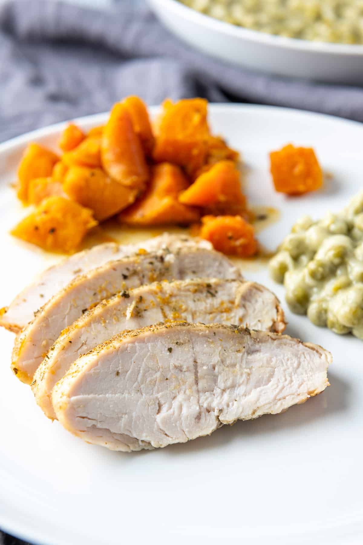 A white plate with slices of turkey, creamed peas, and carrots