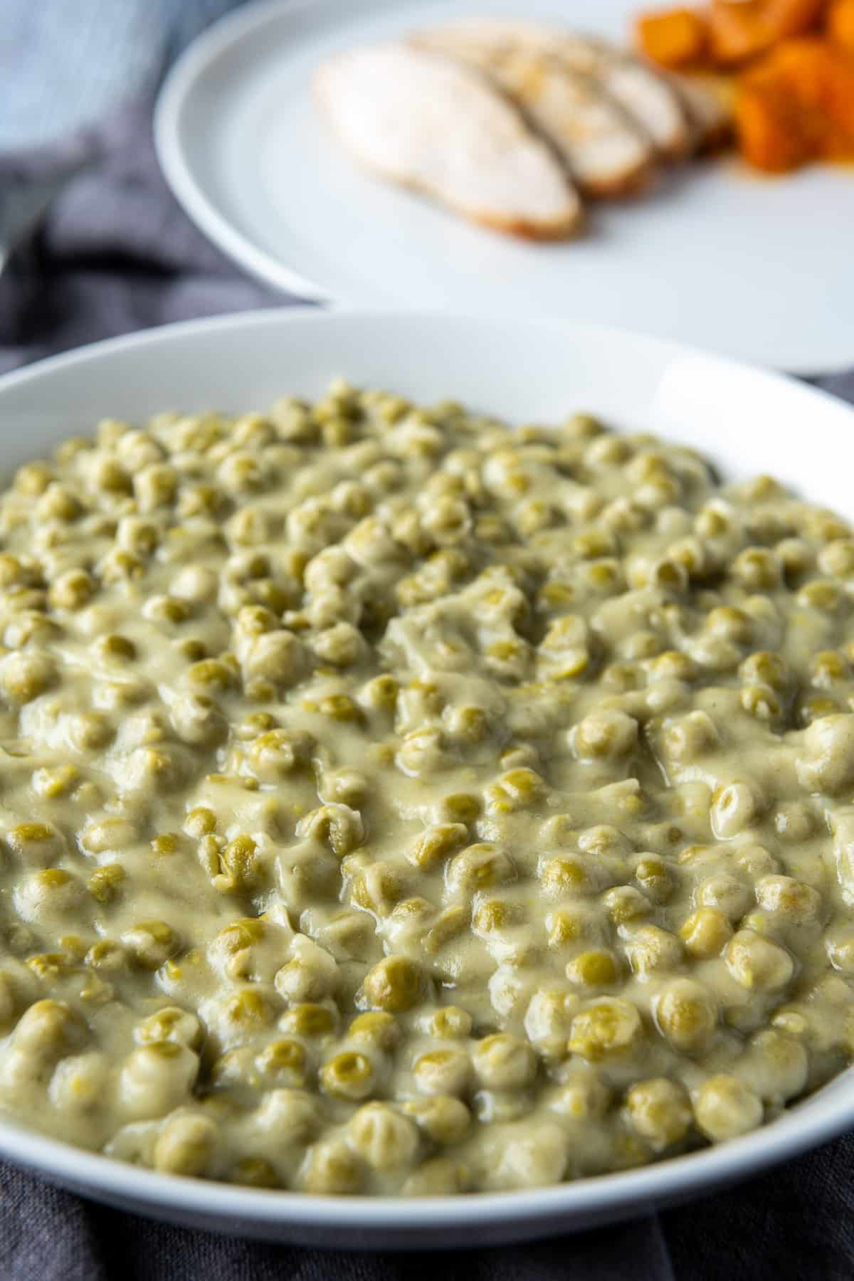 a big deep plate with peas with cream in it - there is also a plate with meat and carrots in back