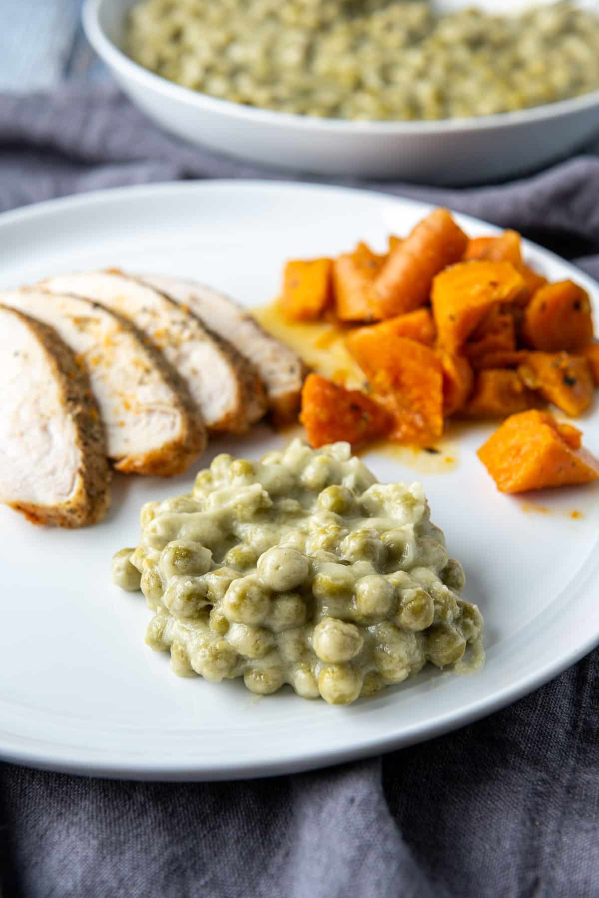 A white plate with creamy peas, carrots and turkey slices