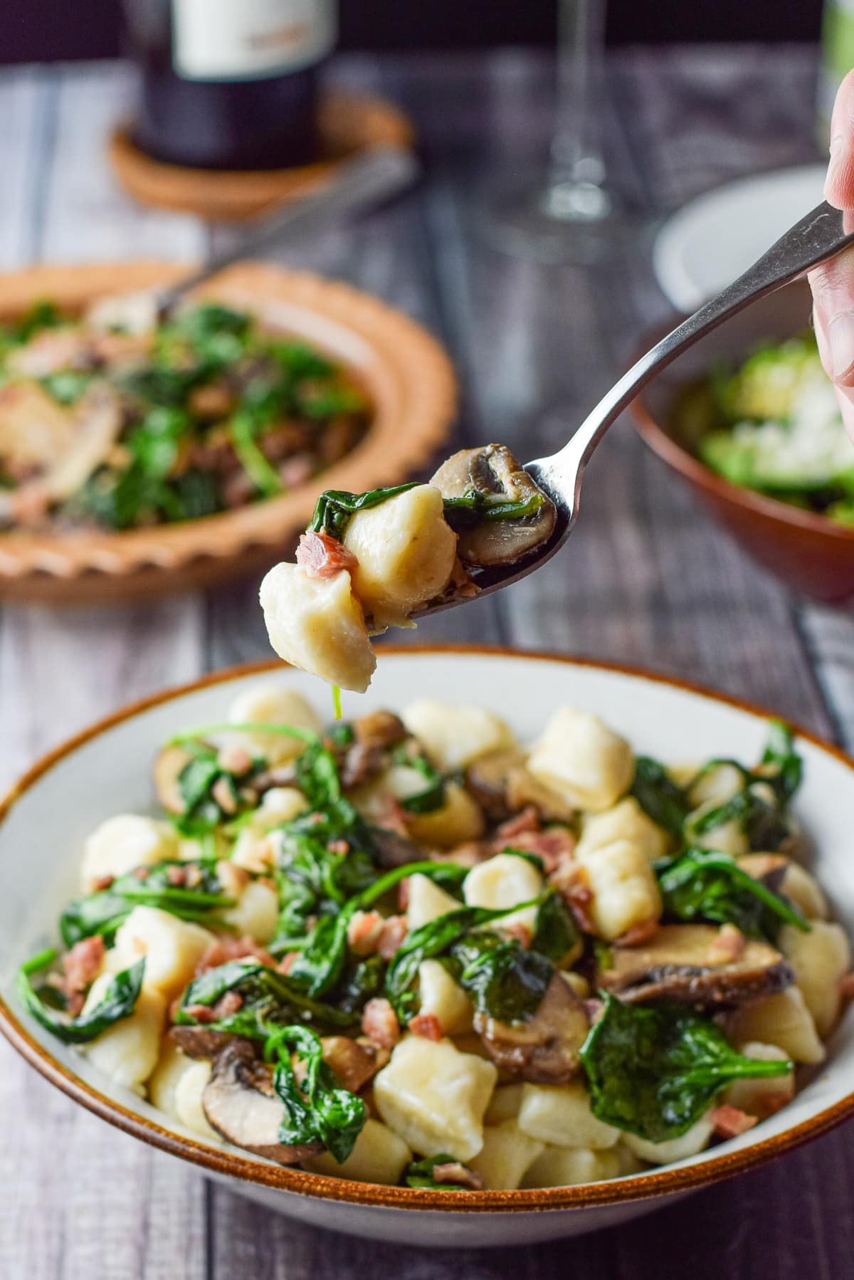 A fork with the gnocchi on it held over the bowl with more veggies in the background