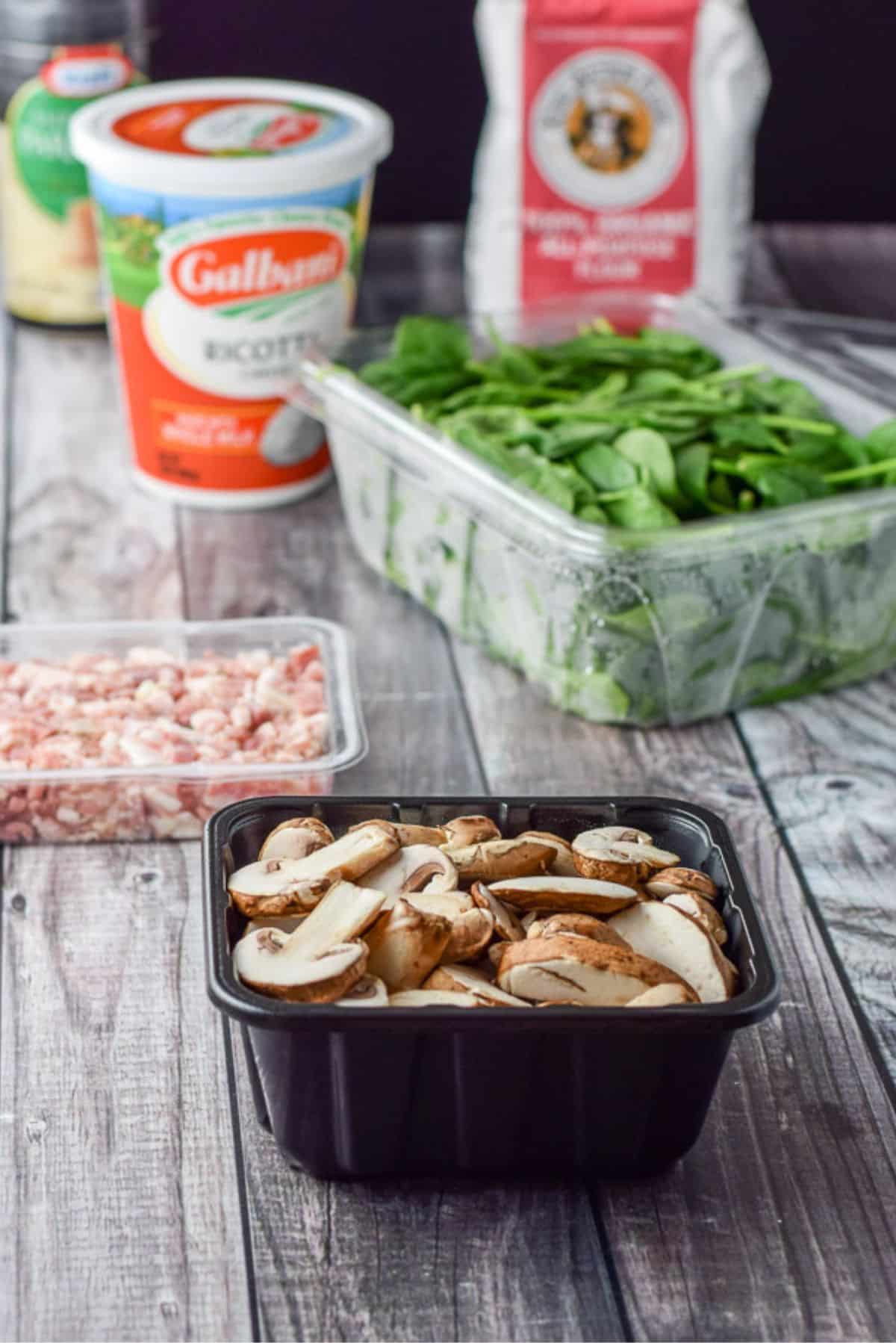 Sliced mushrooms, pancetta, spinach, ricotta, flour and parmesan cheese on a table