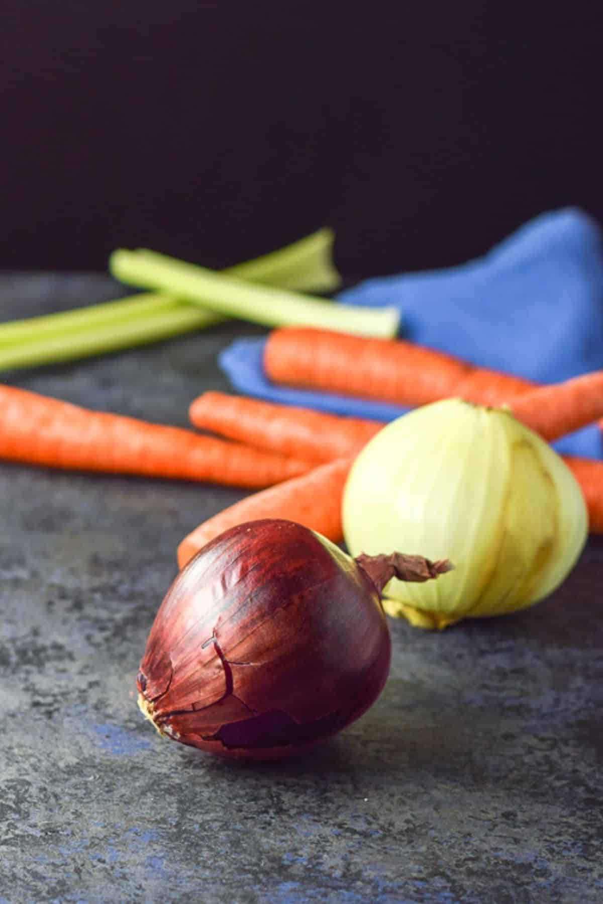 Purple onion, vidalia onion, carrots and celery on a greyish board