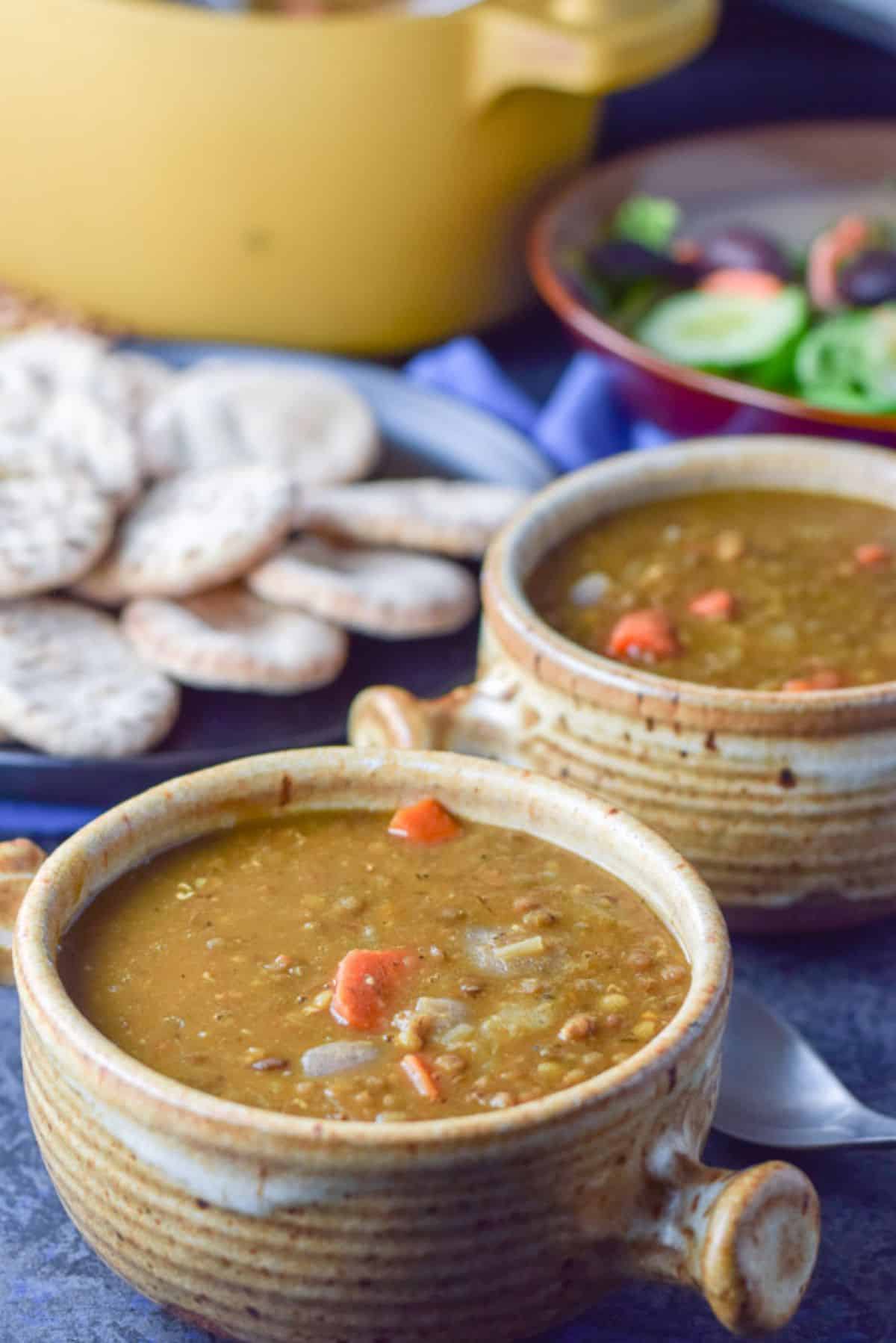 two crocks of lentil soup with a plate of small pita rounds and the big bowl of the soup in the