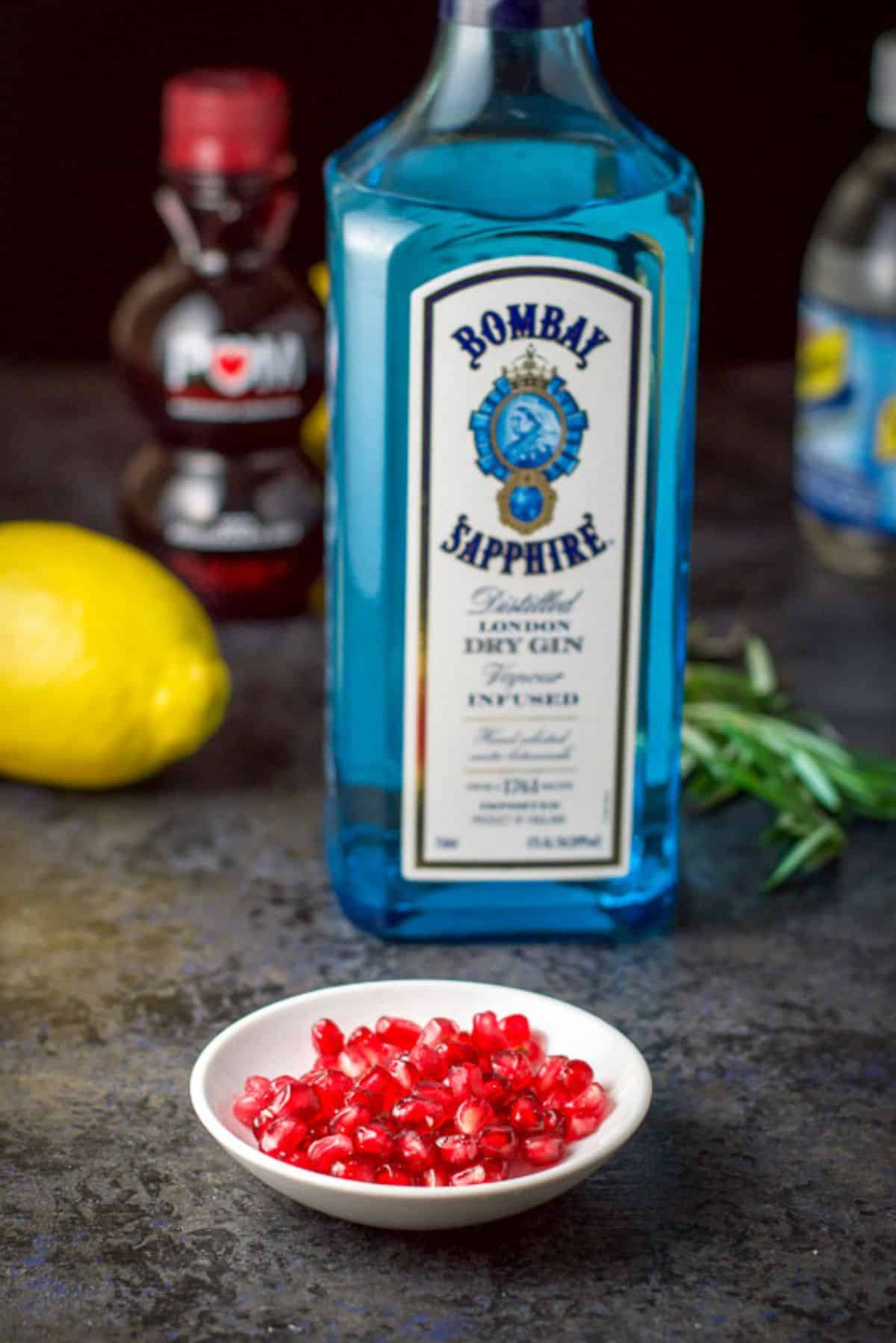 pomegranate seeds, gin, rosemary sprigs, lemon, and pomegranate juice on a table