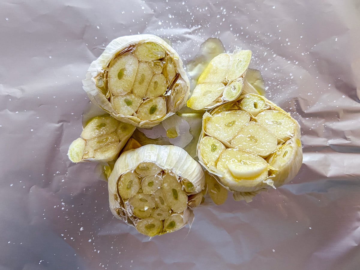 overhead view of raw heads of garlic, oil, and salt on foil