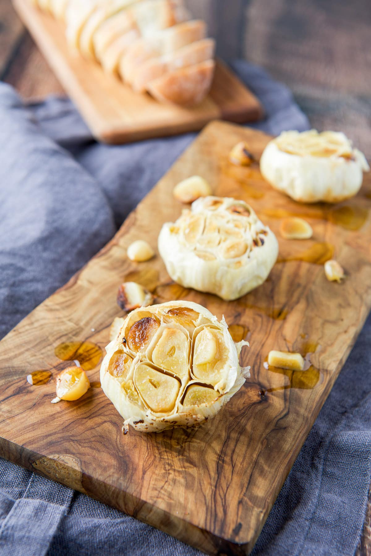 Two wooden boards with heads of cooked garlic and bread