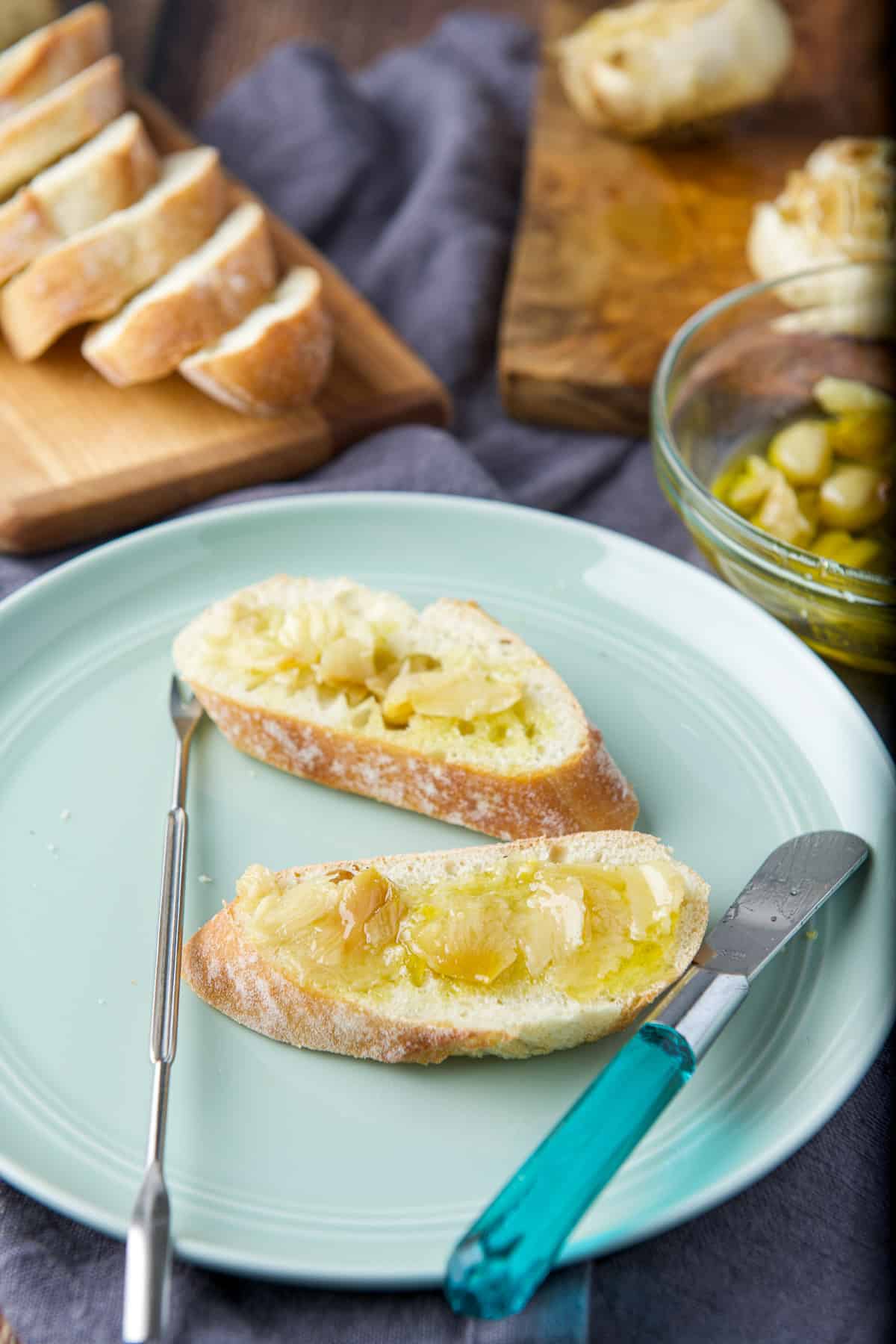 A green plate with two slices of bread with roasted garlic and oil with more bread and garlic in the back
