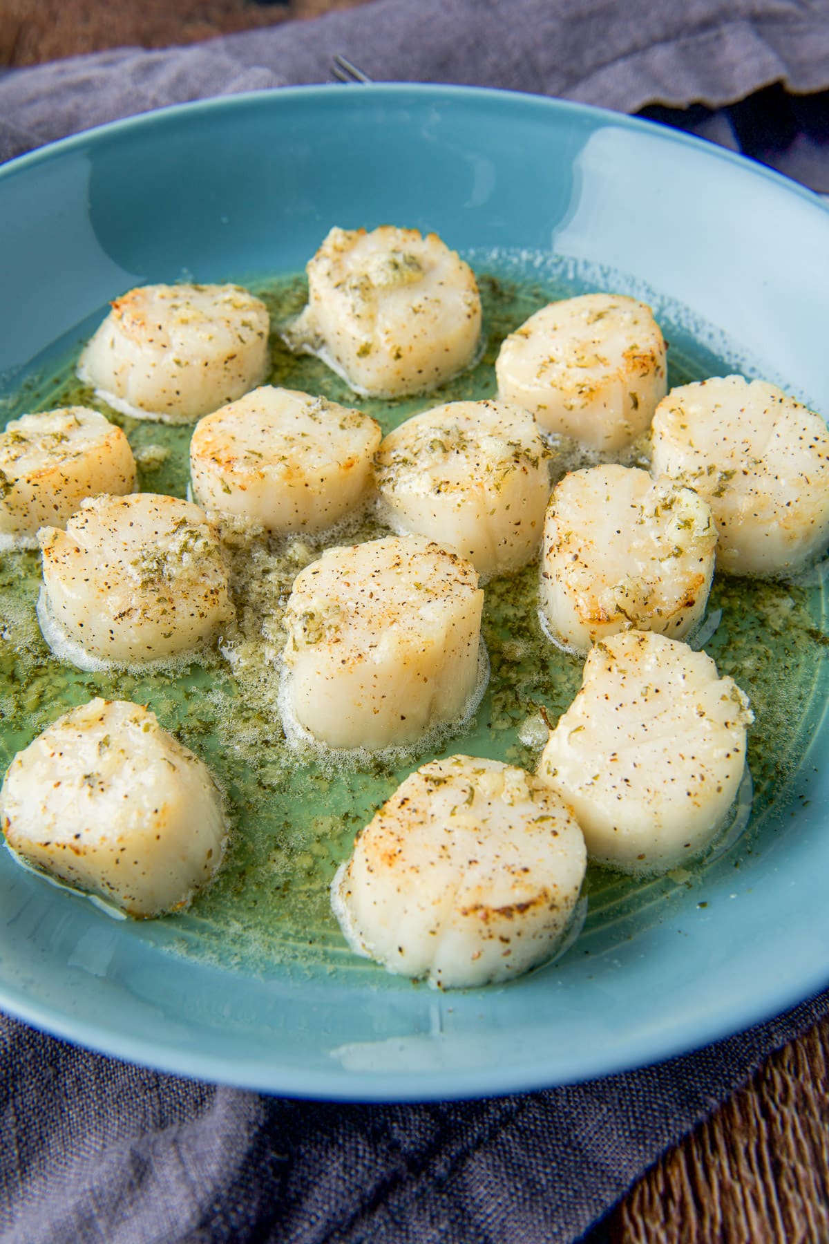 A grey napkin under a blue bowl with the cooked scallops in sauce