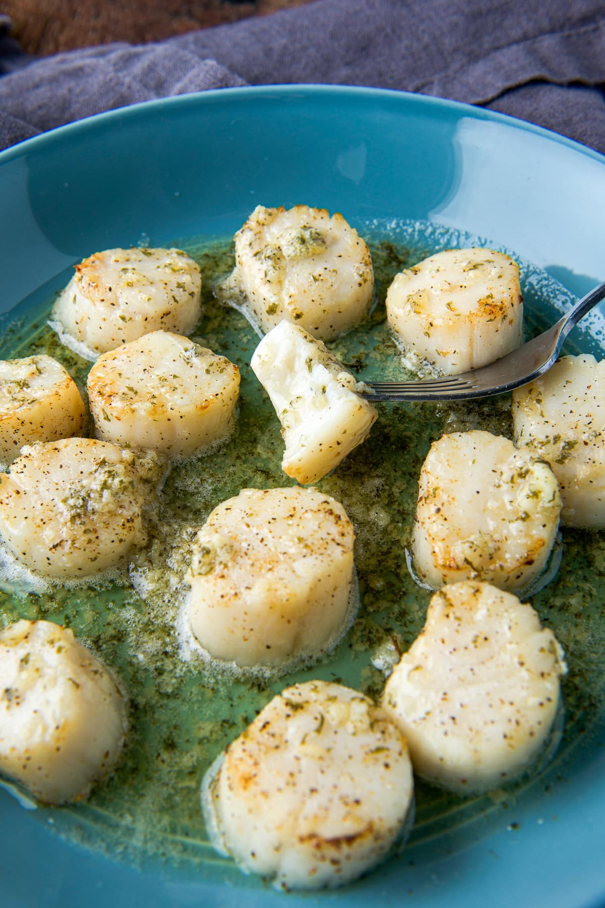 A fork with a scallop with a bite out of it in the dish of other scallops in butter sauce