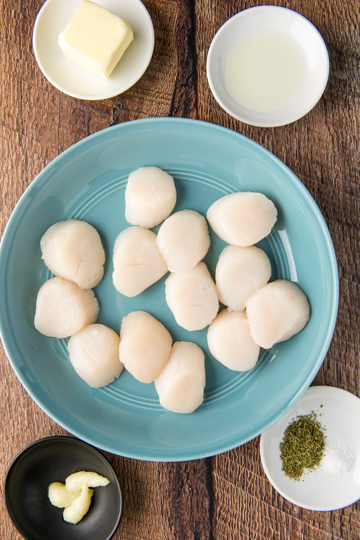 Raw scallops in a deep dish, garlic paste, salt, parsley, butter, and lemon juice