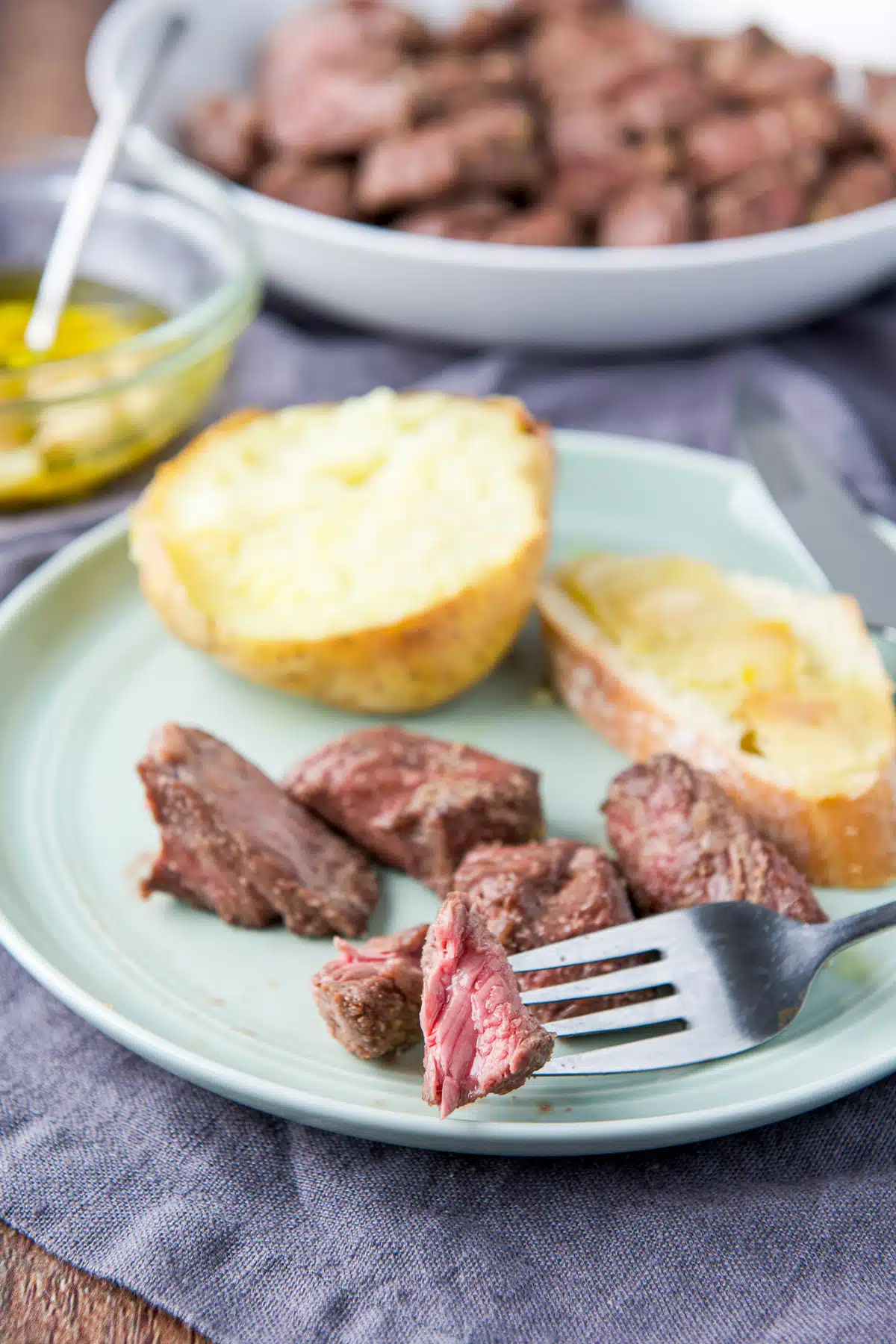 Close up of a fork with a slice of the steak tips on it along with the rest of the tips in the back