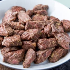 A square photo of a white dish with a pile of steak tips on it