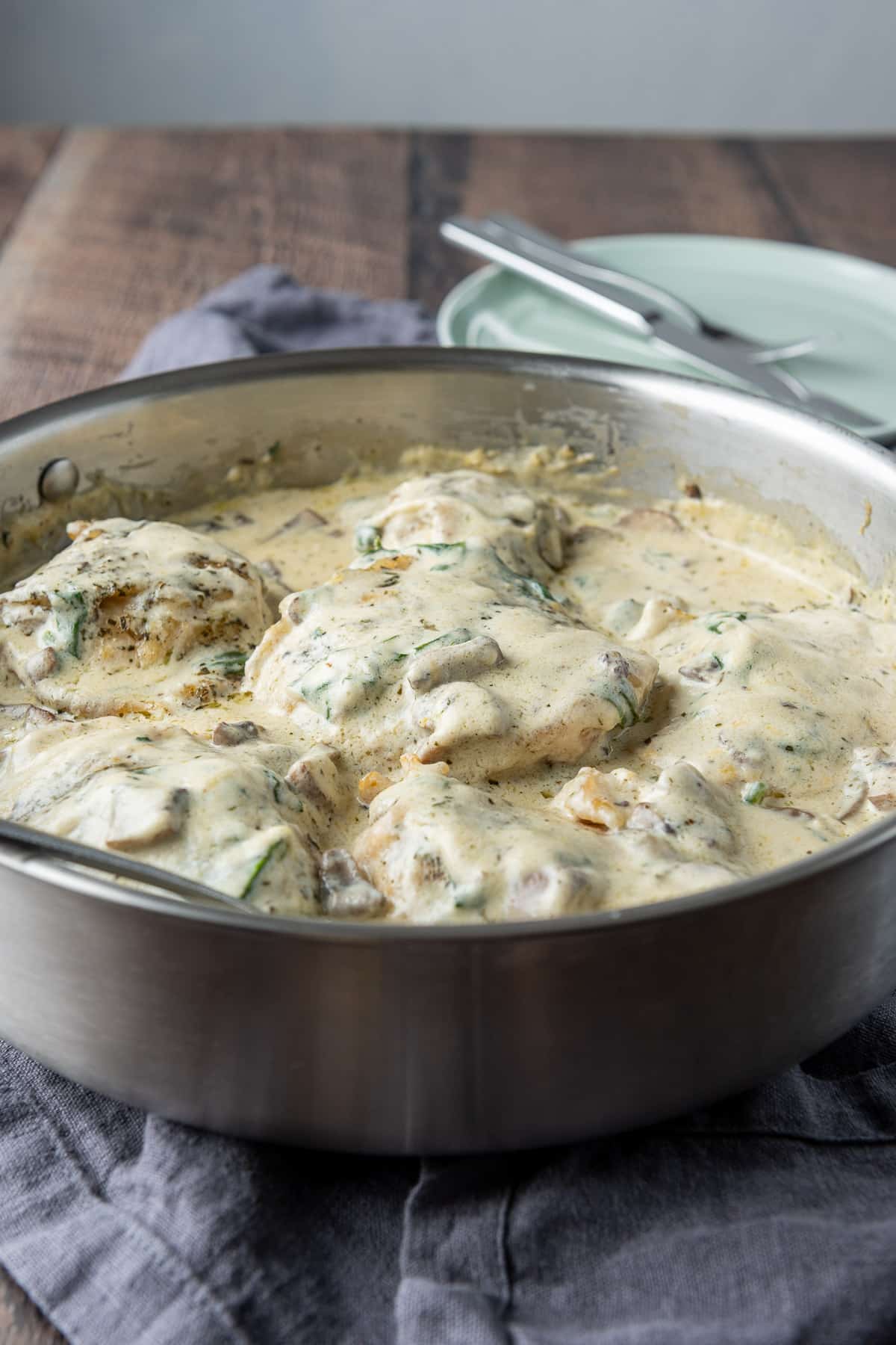 A wooden table with a pan of creamy chicken on it. There is also a green plate with a knife and fork