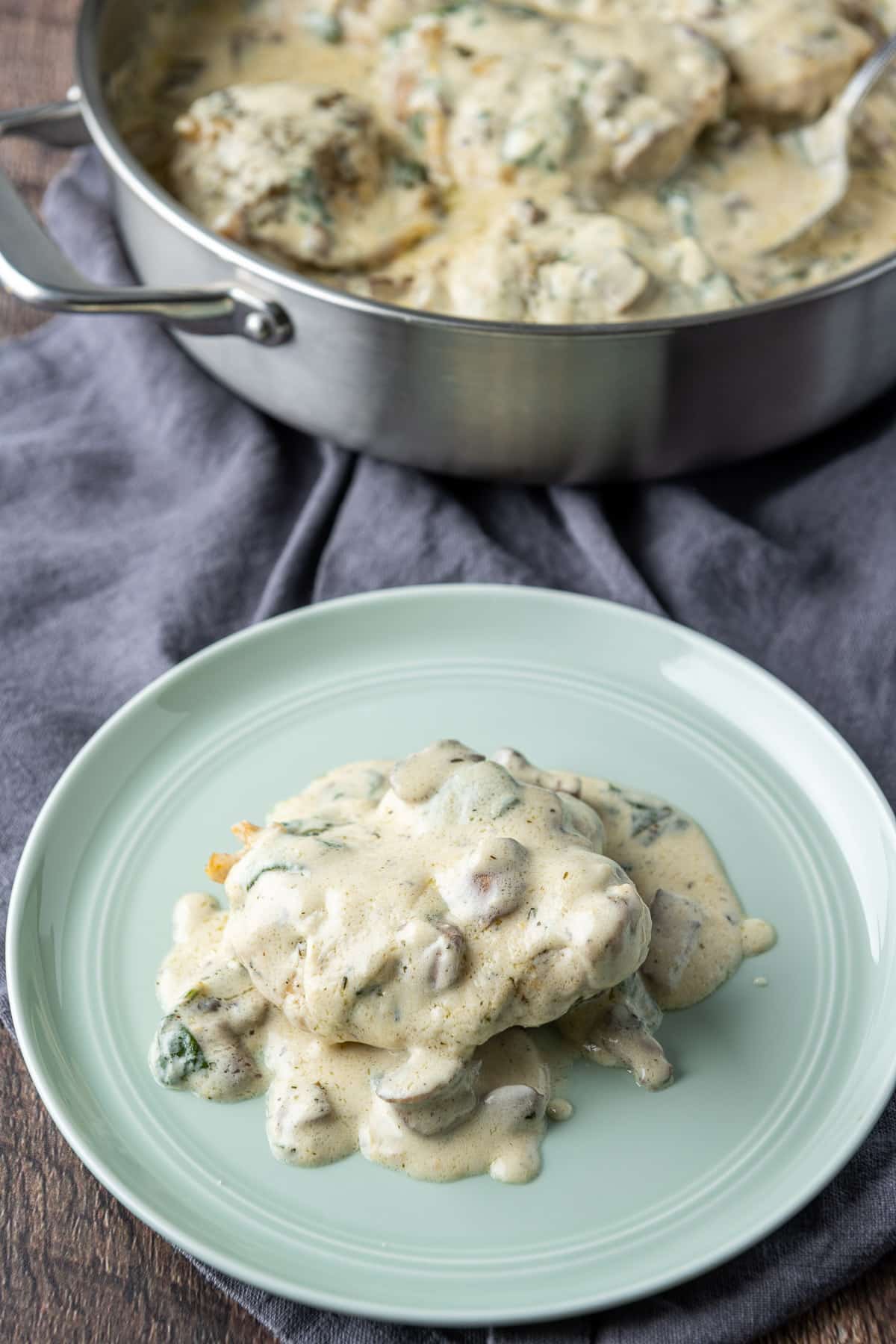 A green plate with a chicken thigh on it with the creamy sauce over it. The pan of chicken is in the background