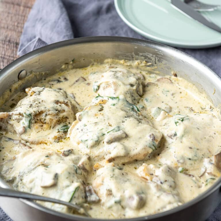 A square photo of a metal pan with a creamy sauce on chicken