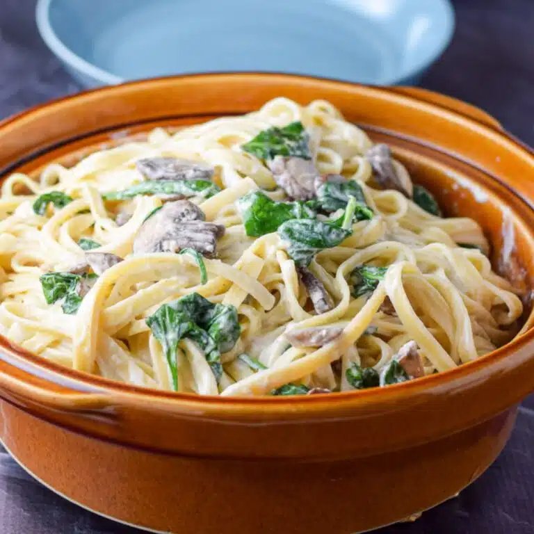 A square photo of a brown bowl with creamy fettuccine with vegetables