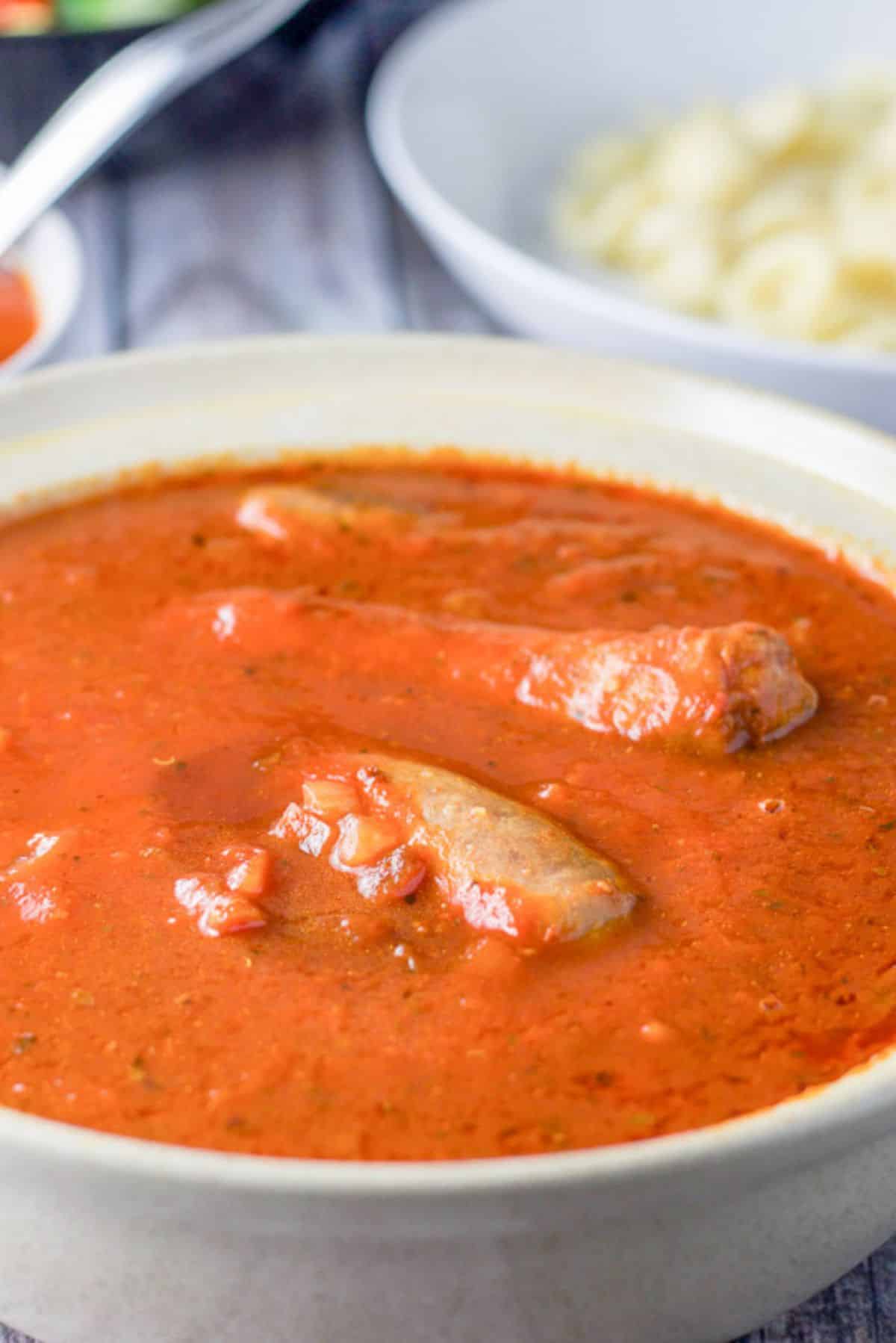 Sausages peaking out of a serving bowl with pasta in a bowl behind it