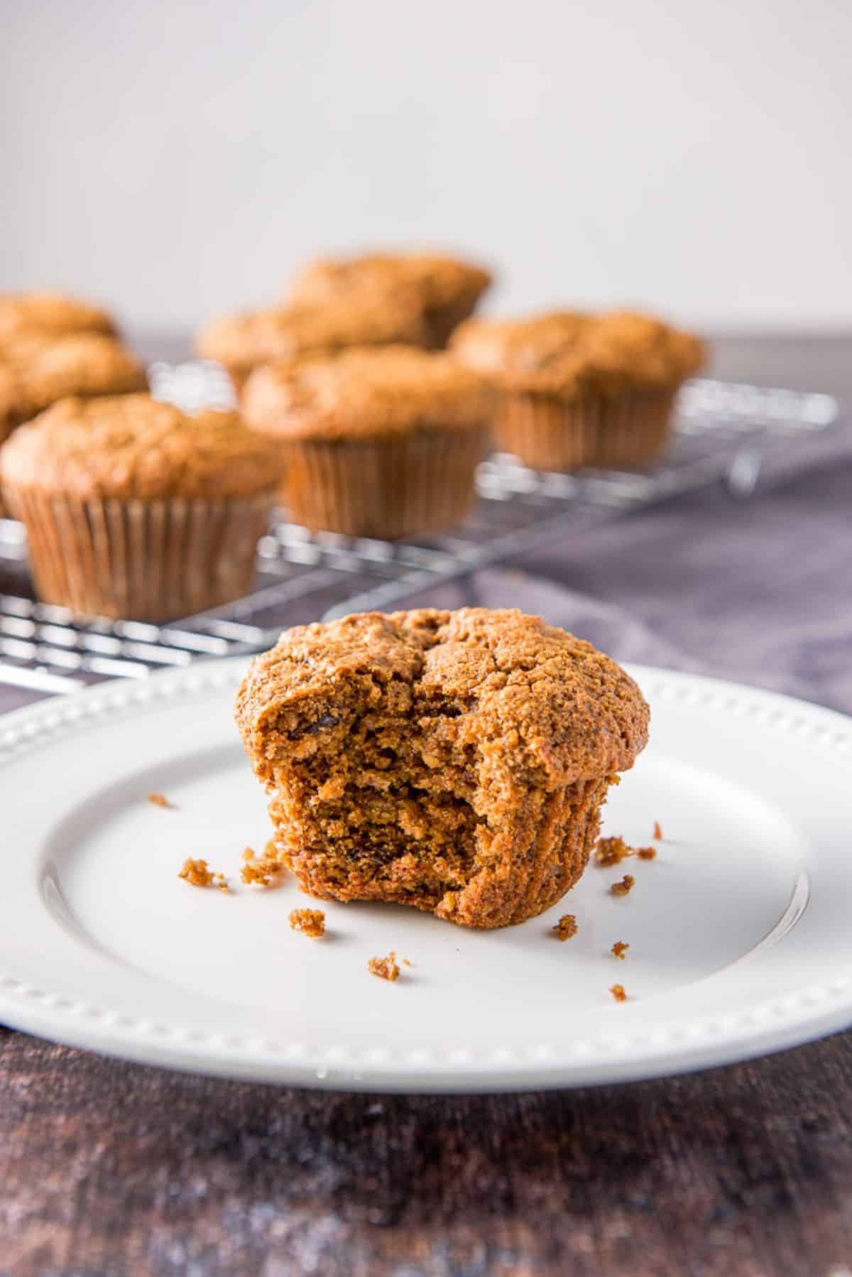 A white plate with a bite out of one of the oat bran muffins. There are more muffins in the back