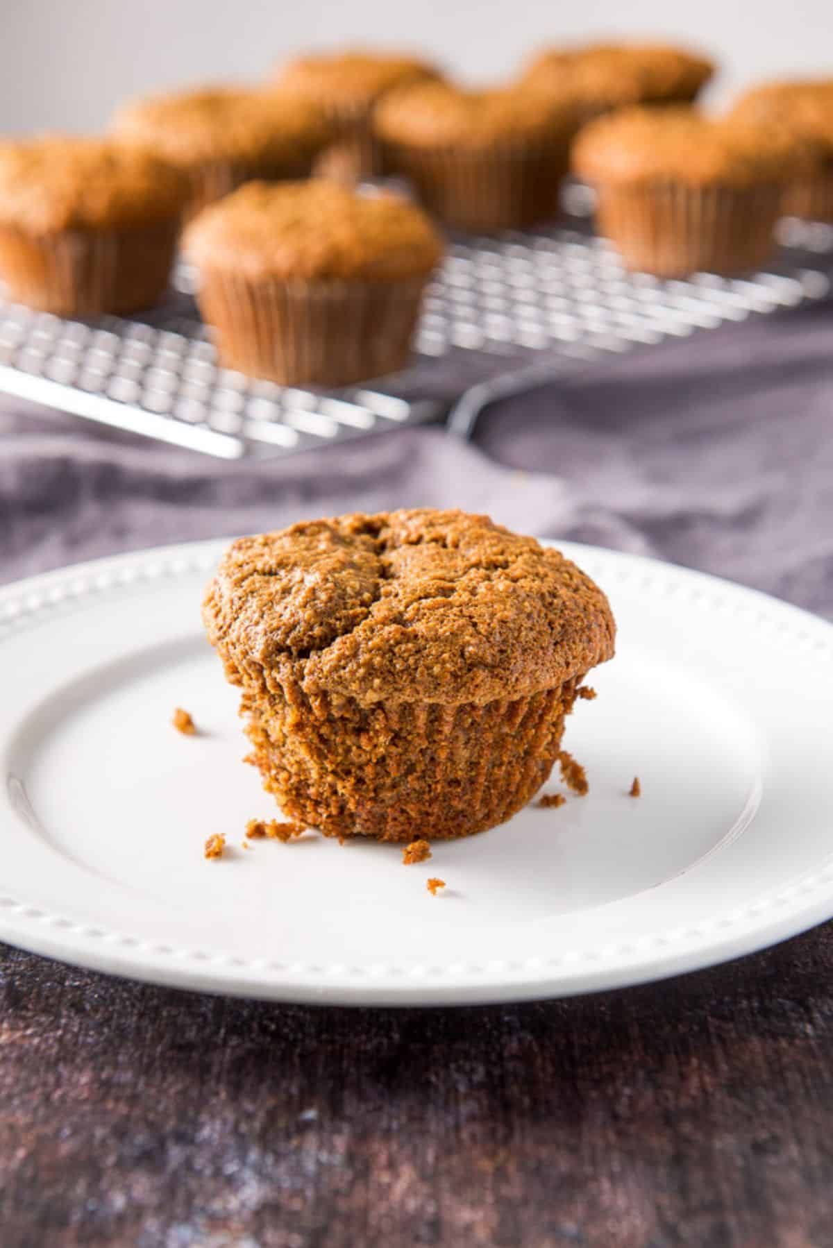 Close up of one of the oat bran muffins on a white plate with more muffins in the background