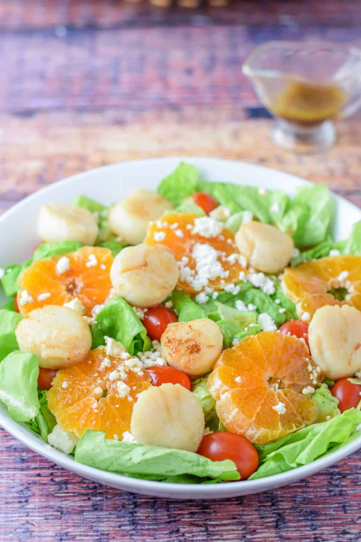 Closer look at the white shallow bowl with the scallops on the salad