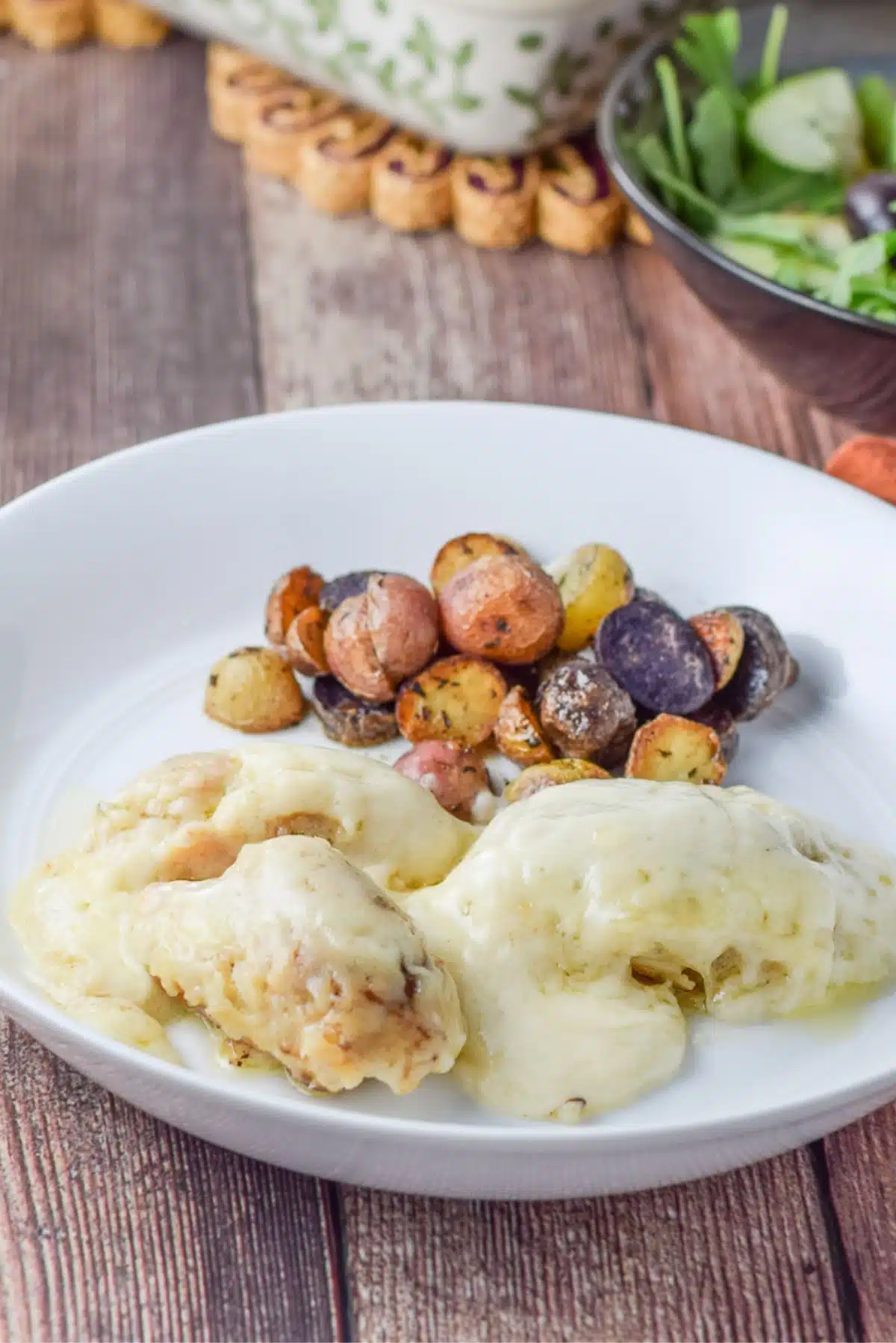 A deep dish with two pieces of chicken with swiss cheese on it. There is the baking dish in the background as well as a salad