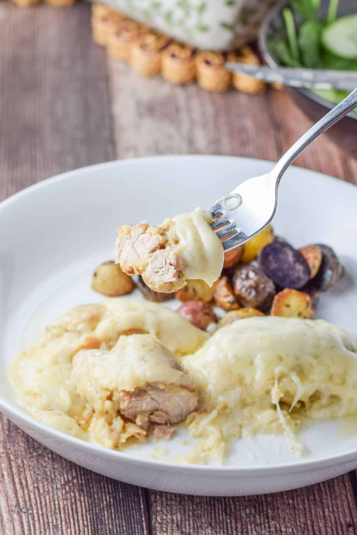 Close view of a forkful of chicken with a dollop of cheese on it over a white plate with the meal