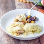 A forkful of chicken with a dollop of cheese on it over a white plate with the meal - square