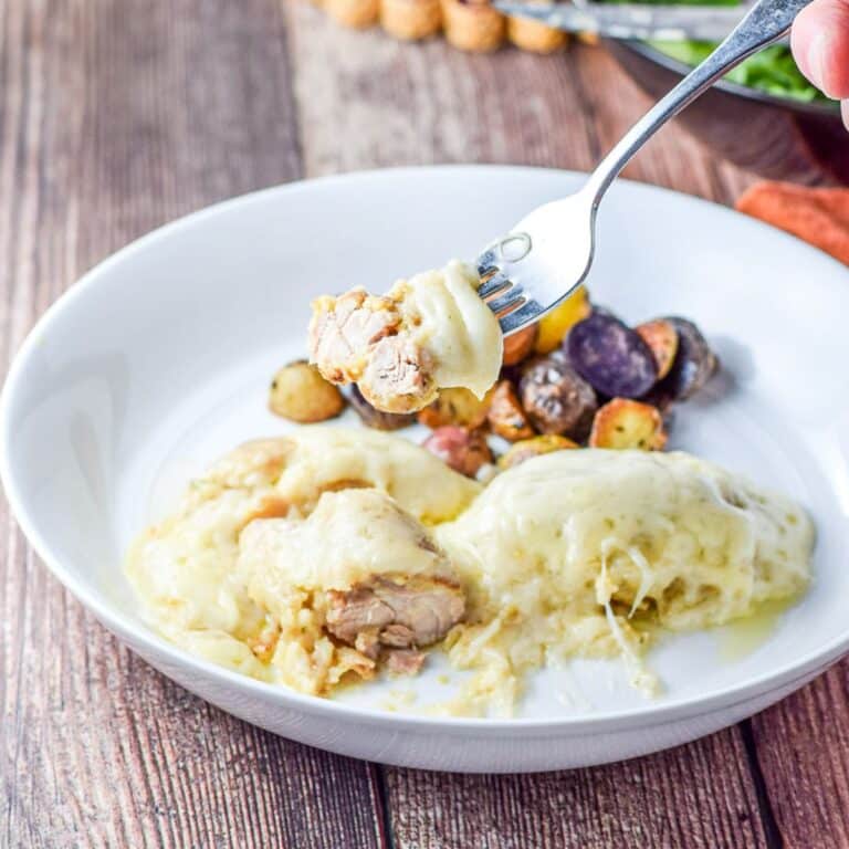 A forkful of chicken with a dollop of cheese on it over a white plate with the meal - square