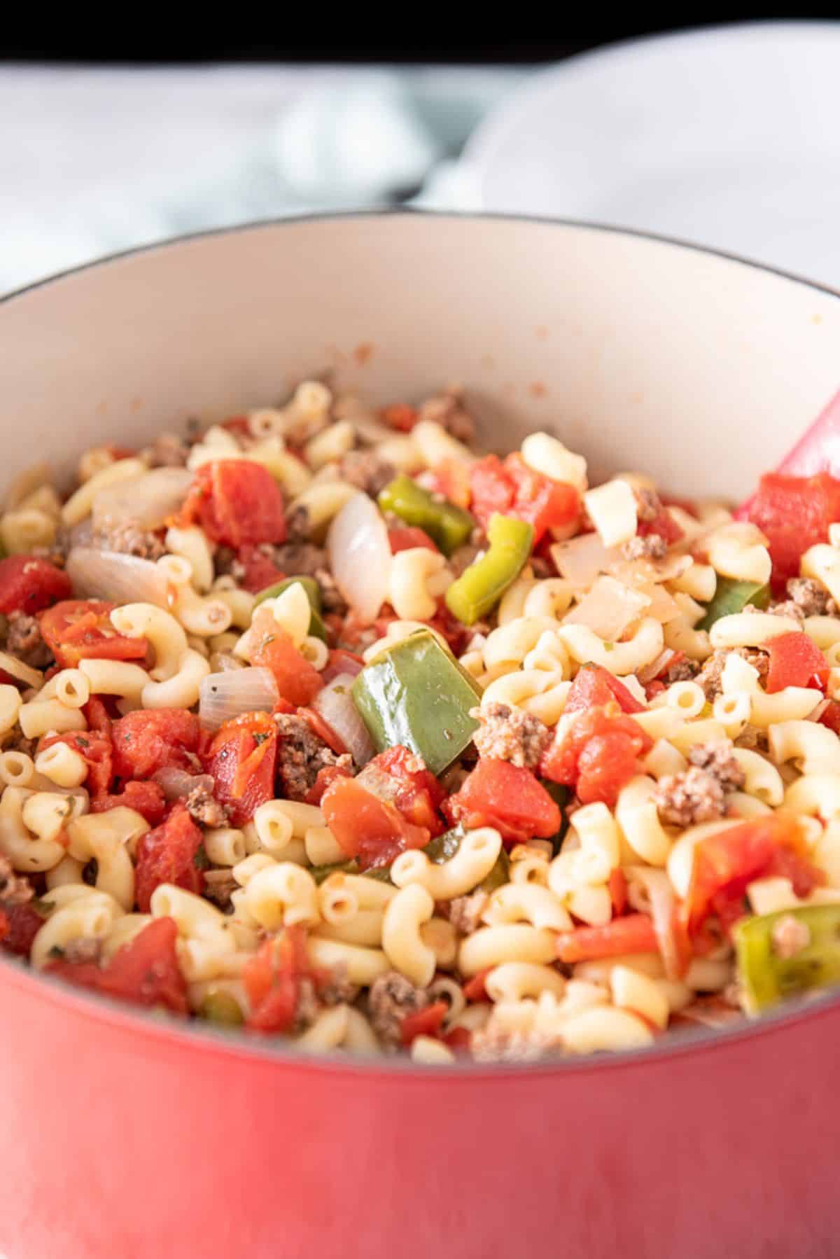 A big red pan full of elbow macaroni, ground beef, tomatoes, peppers and onions