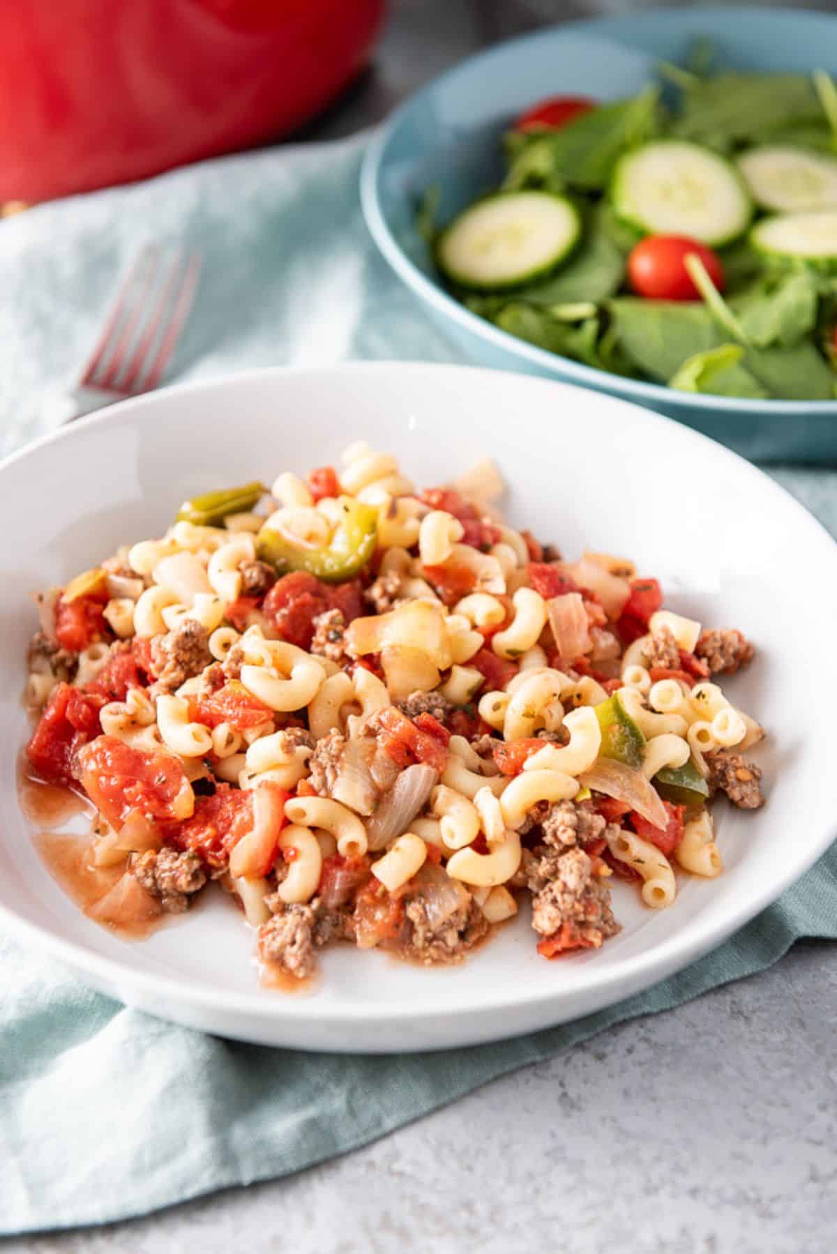 Big bowl of chop suey in a shallow bowl, with a salad in the background