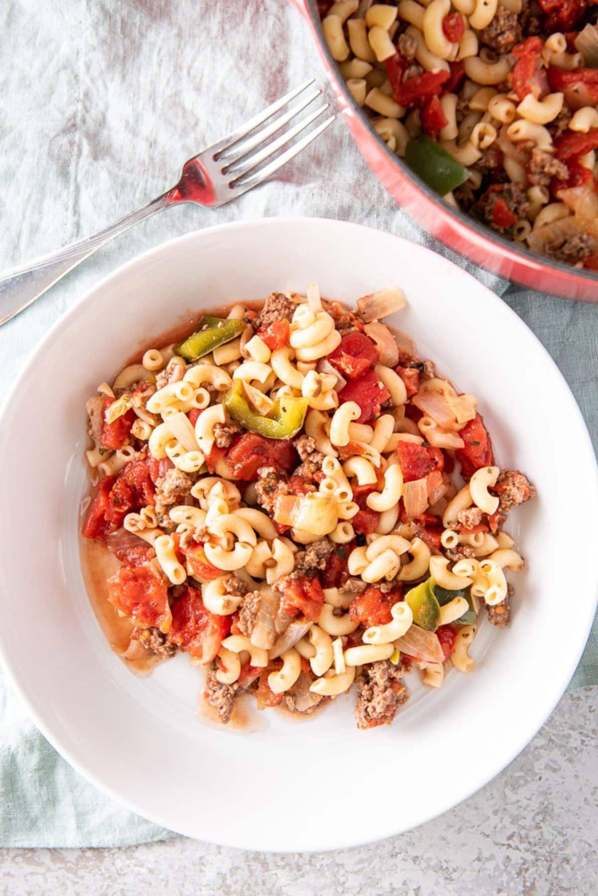 Overhead view of bowl of noodles and sauce. It's on a napkin, fork and a big pan of the dish