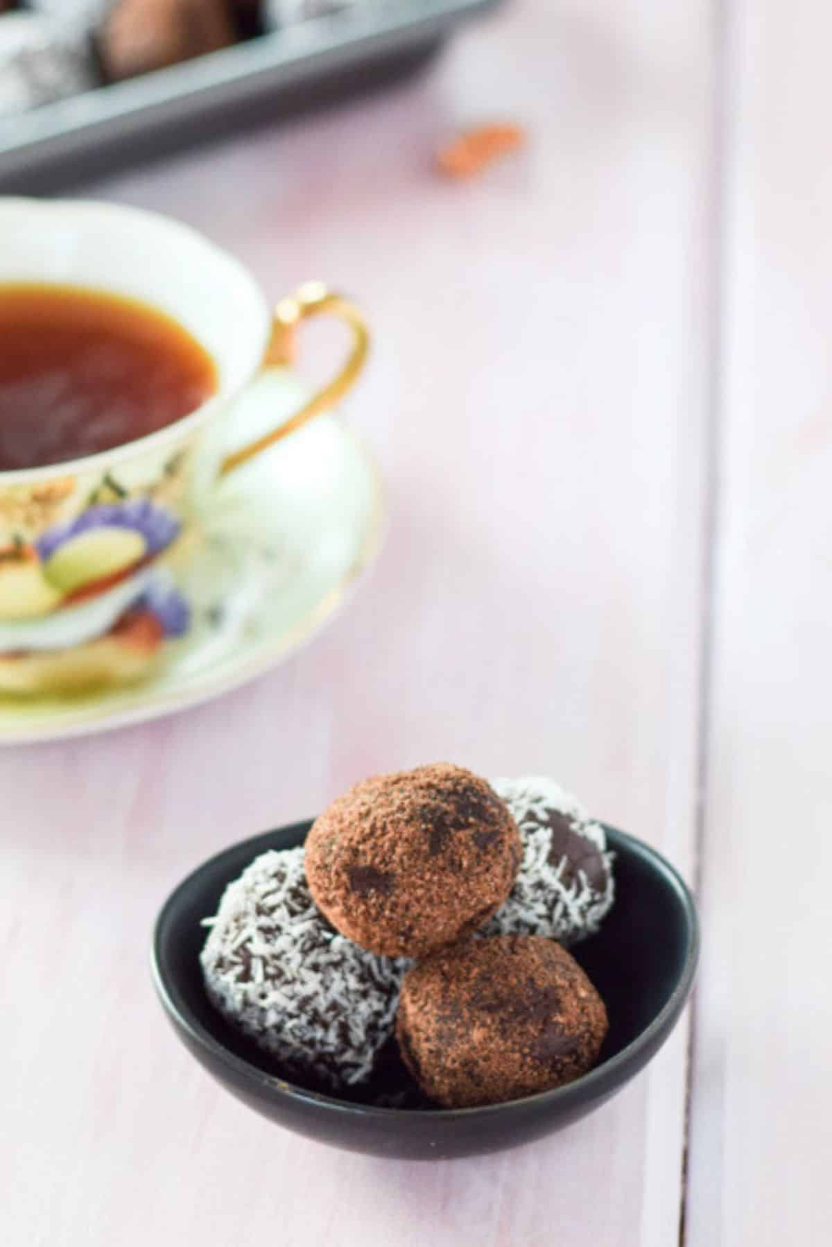 Four rum balls piled in a small black bowl, with tea and the rest of the balls in the back