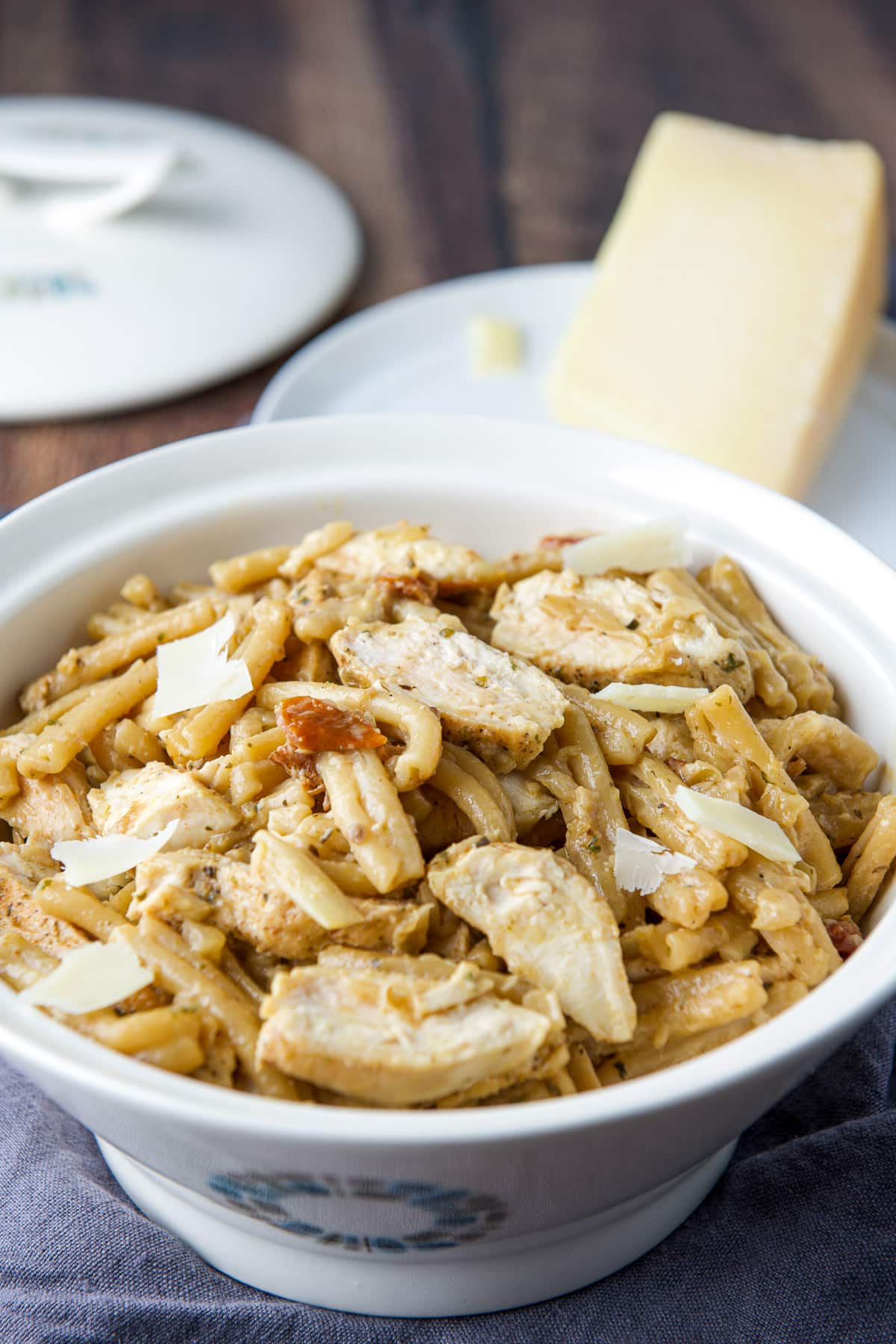 A plate of parmesan behind a white bowl with the chicken pasta