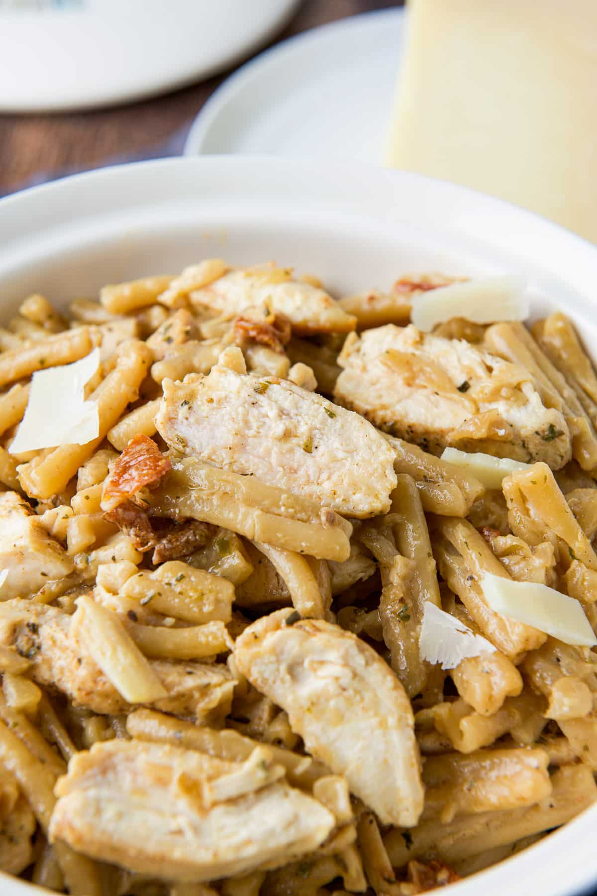 Sliced chicken on pasta with a sauce and cheese in the back