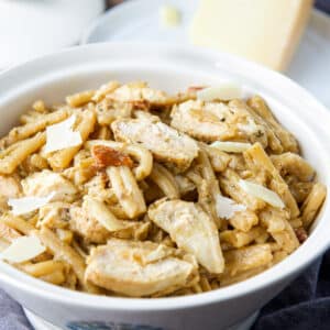 square photo of a white bowl with chicken, pasta, and cheese