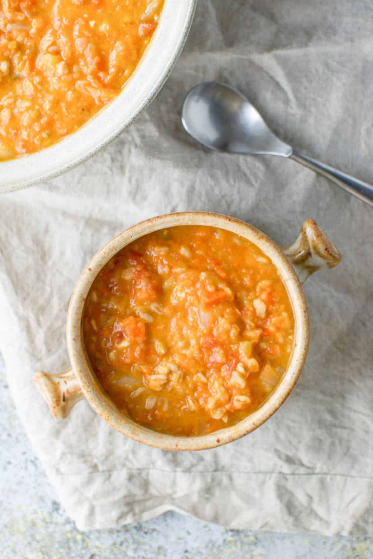Overhead view of the crock of white bean soup with a spoon and big bowl in the background