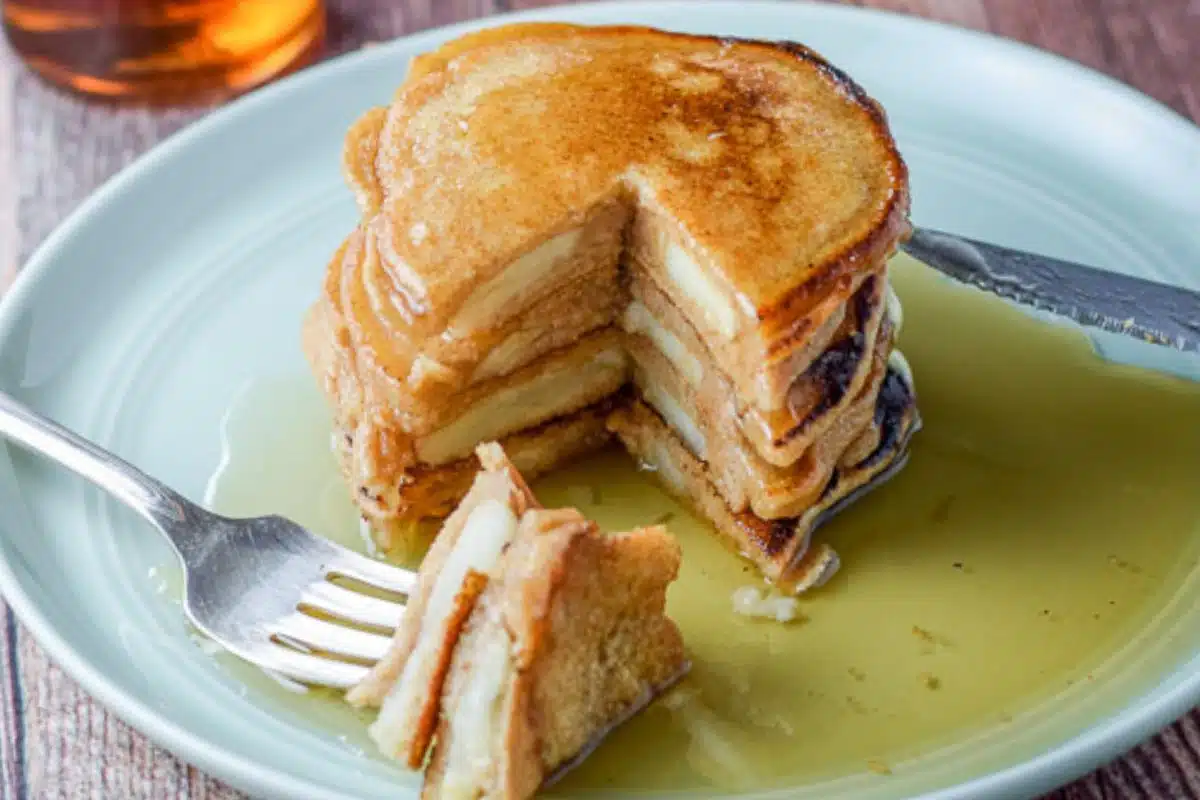 horizontal photo of a green plate with a stack of apple pancakes on it in a puddle of maple syrup