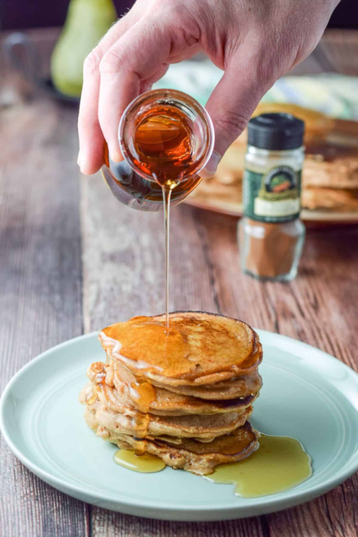 A male hand holding a bottle of syrup being poured on the stack of apple pancakes