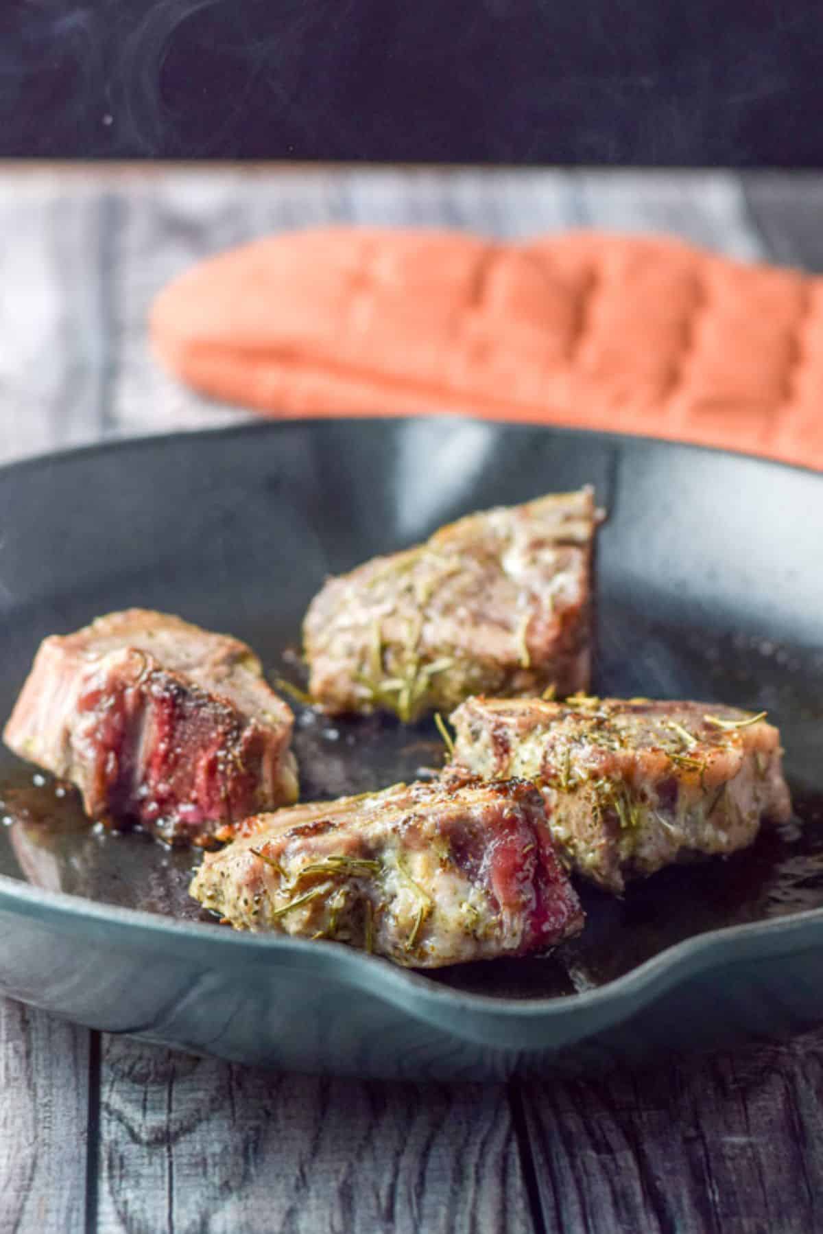 Four lamb chops seared in a pan on a table with an oven mitt.