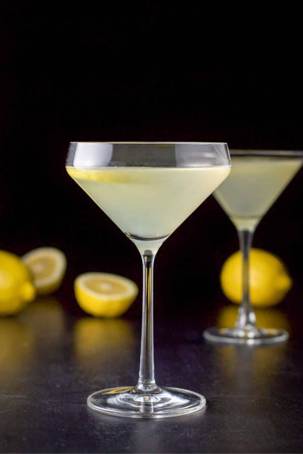 Curved martini glass in vertical view with the cocktail in it with lemons on the table