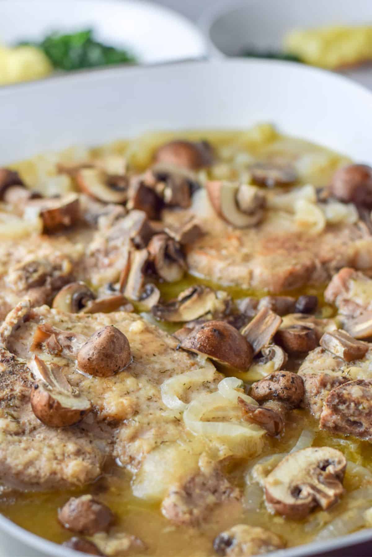 The pan with the pork chops, onions, and mushrroms in a sauce