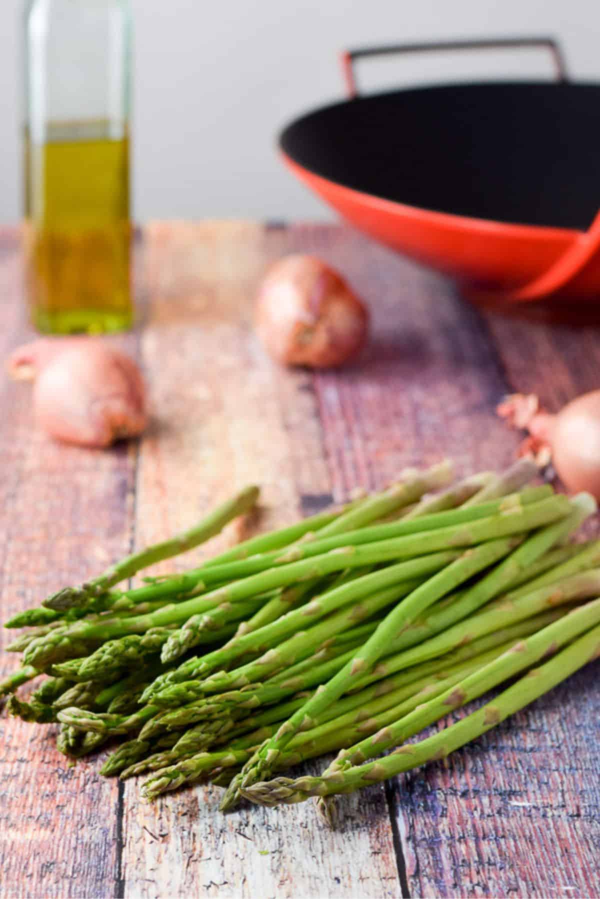 Asparagus, shallots, olive oil and a wok on a wooden table