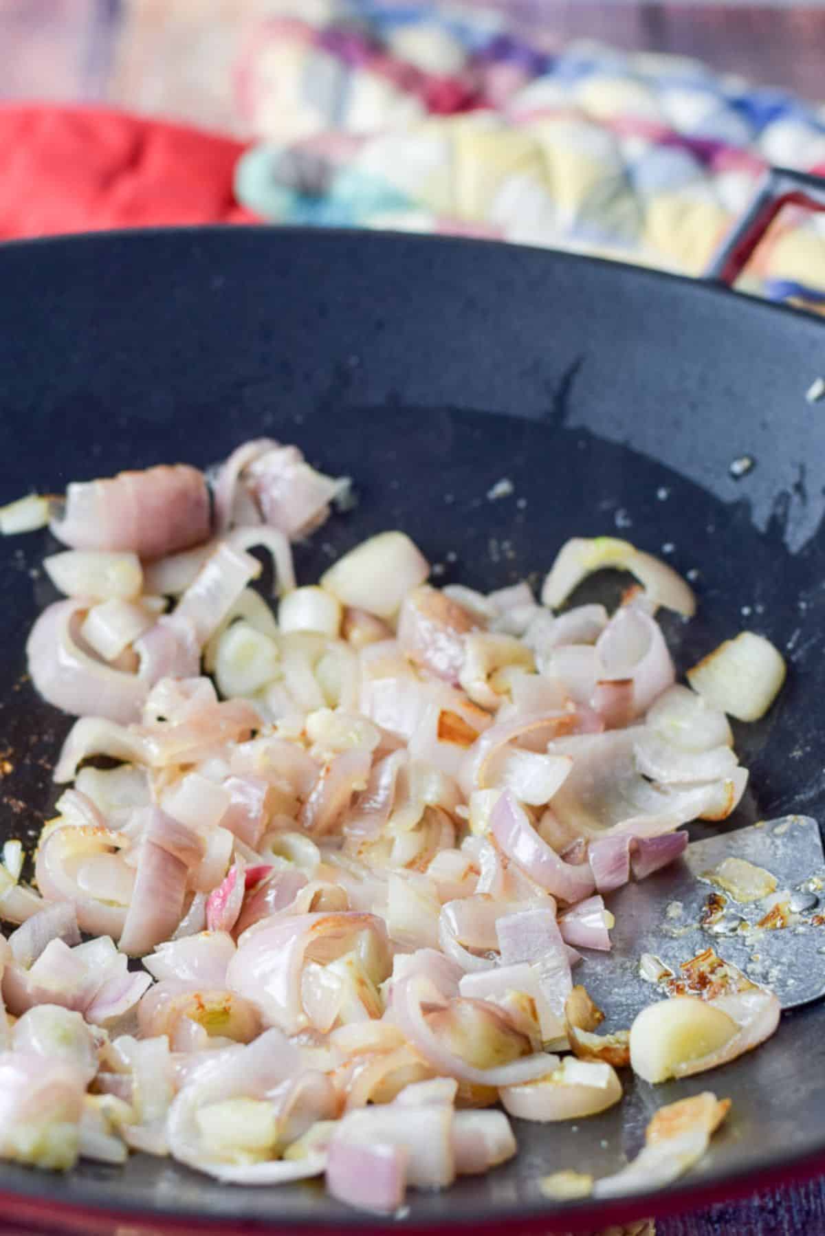 Shallots saut&eacute;d in a wok with a few oven mitts in the background