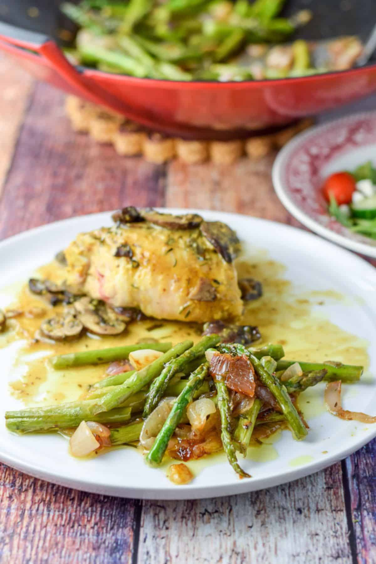 Asparagus and onion plated with some chicken with mushrooms. There is a salad and wok with the veggie in it in the background