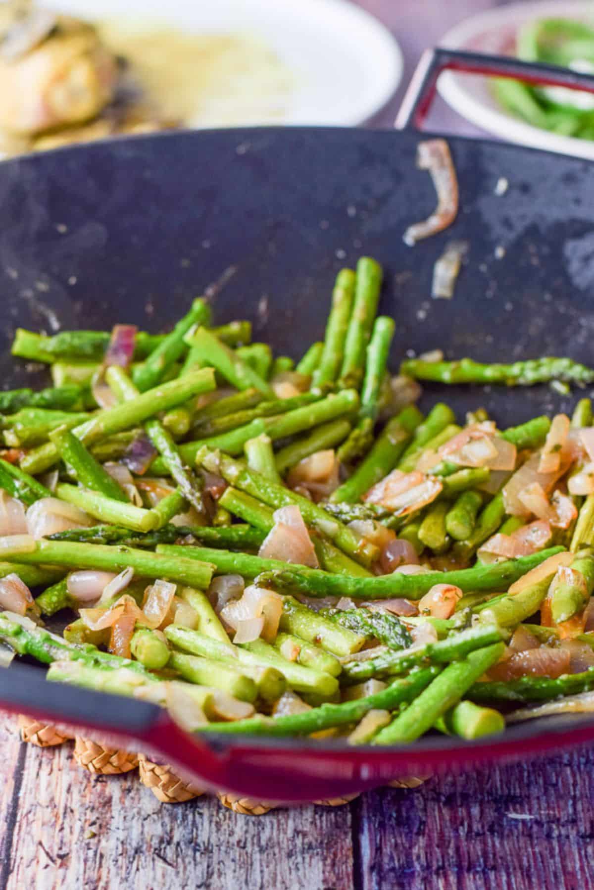 Asparagus in the wok completely cooked with a plate of chicken in the background