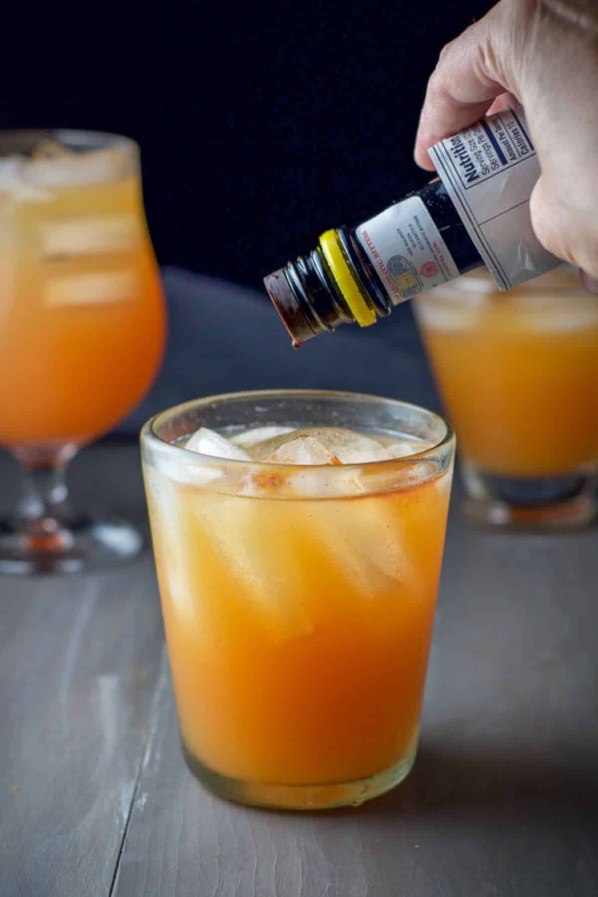 A hand holding a bitters bottle over a cocktail letting the drops fall into the glass