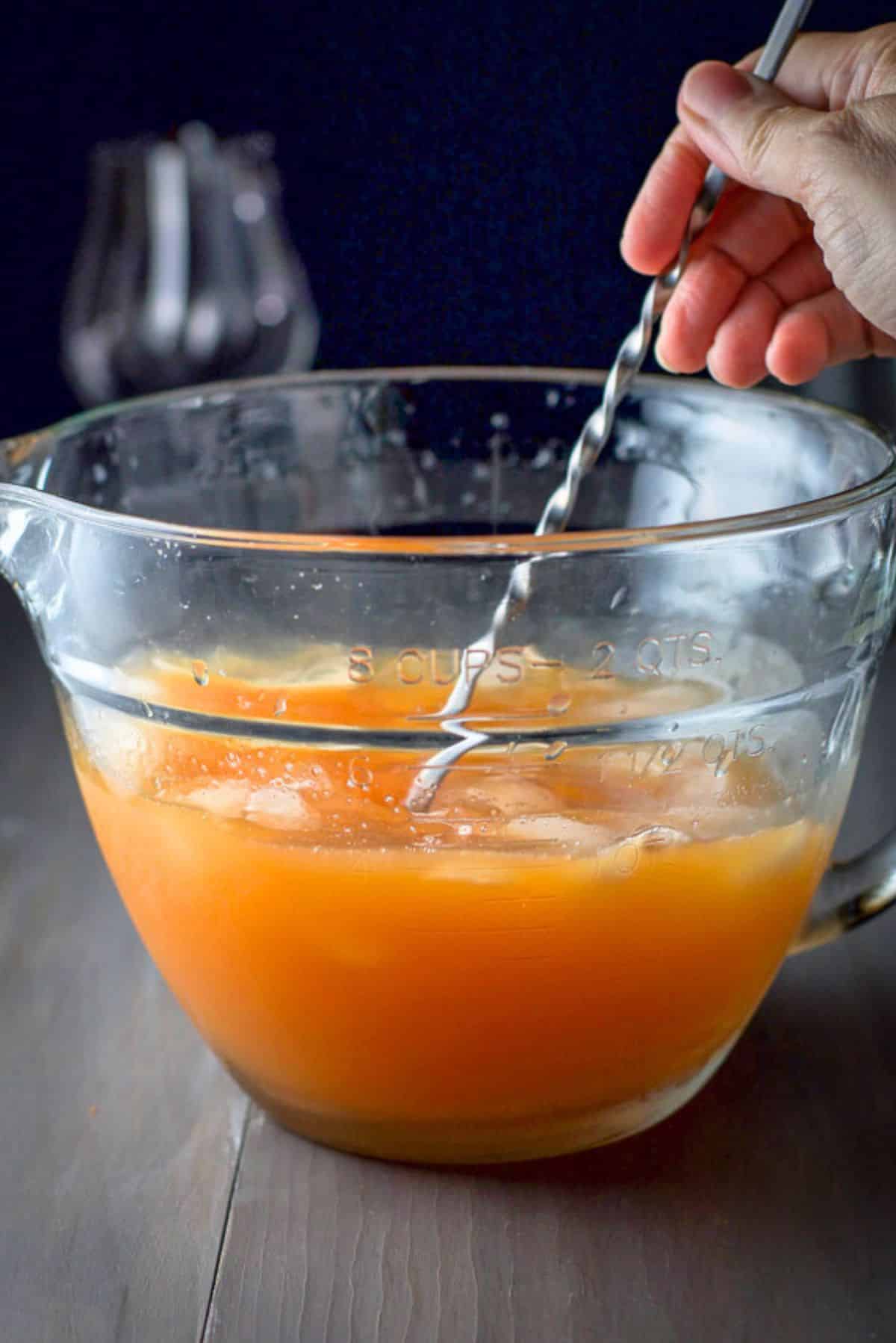 A hand holding a spoon in a big glass bowl with the cocktail in it