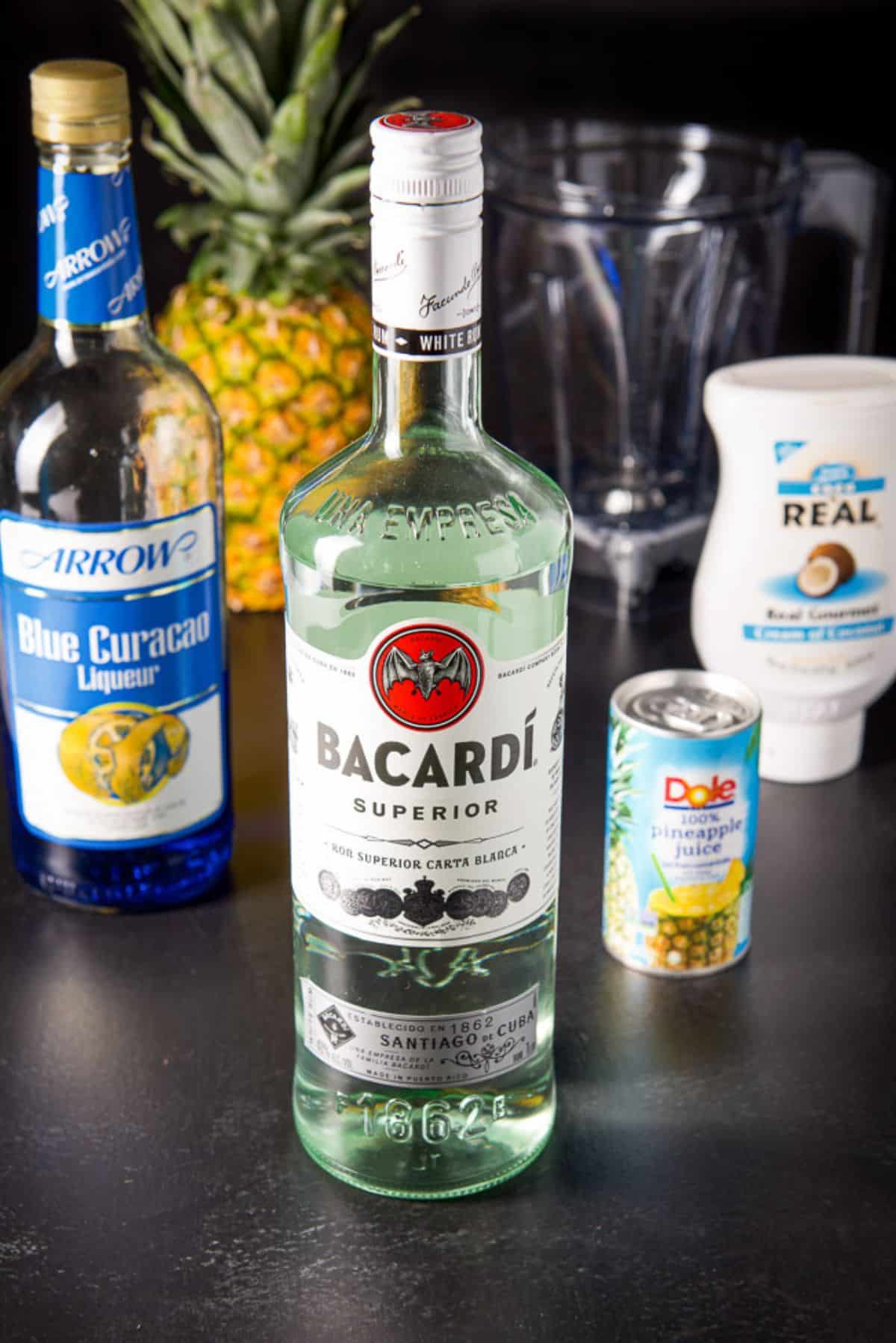 Rum, blue curacao, creme de coconut and pineapple juice with a pineapple in the background along with glassware