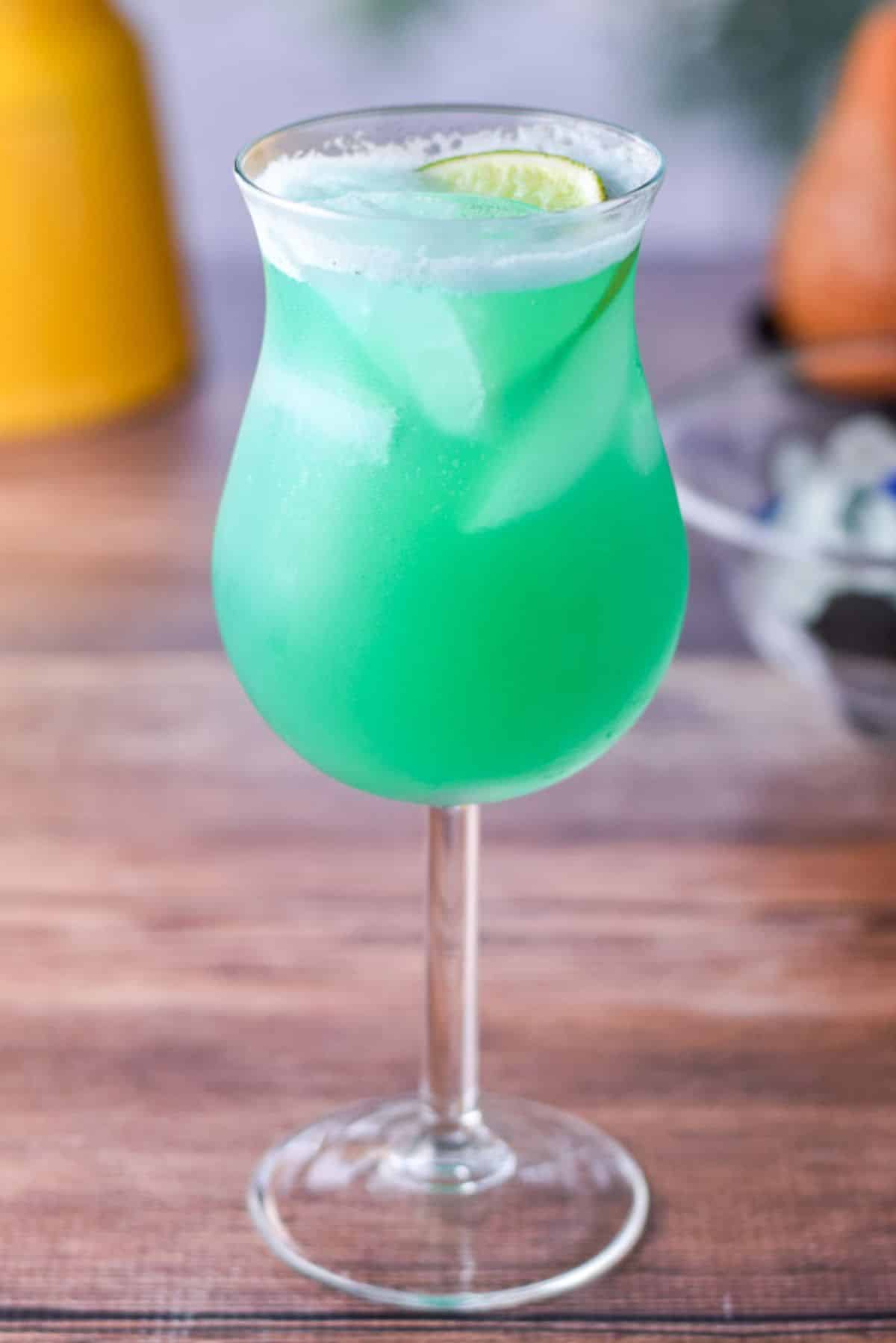 A blue-green cocktail in a tulip glass on a wooden table