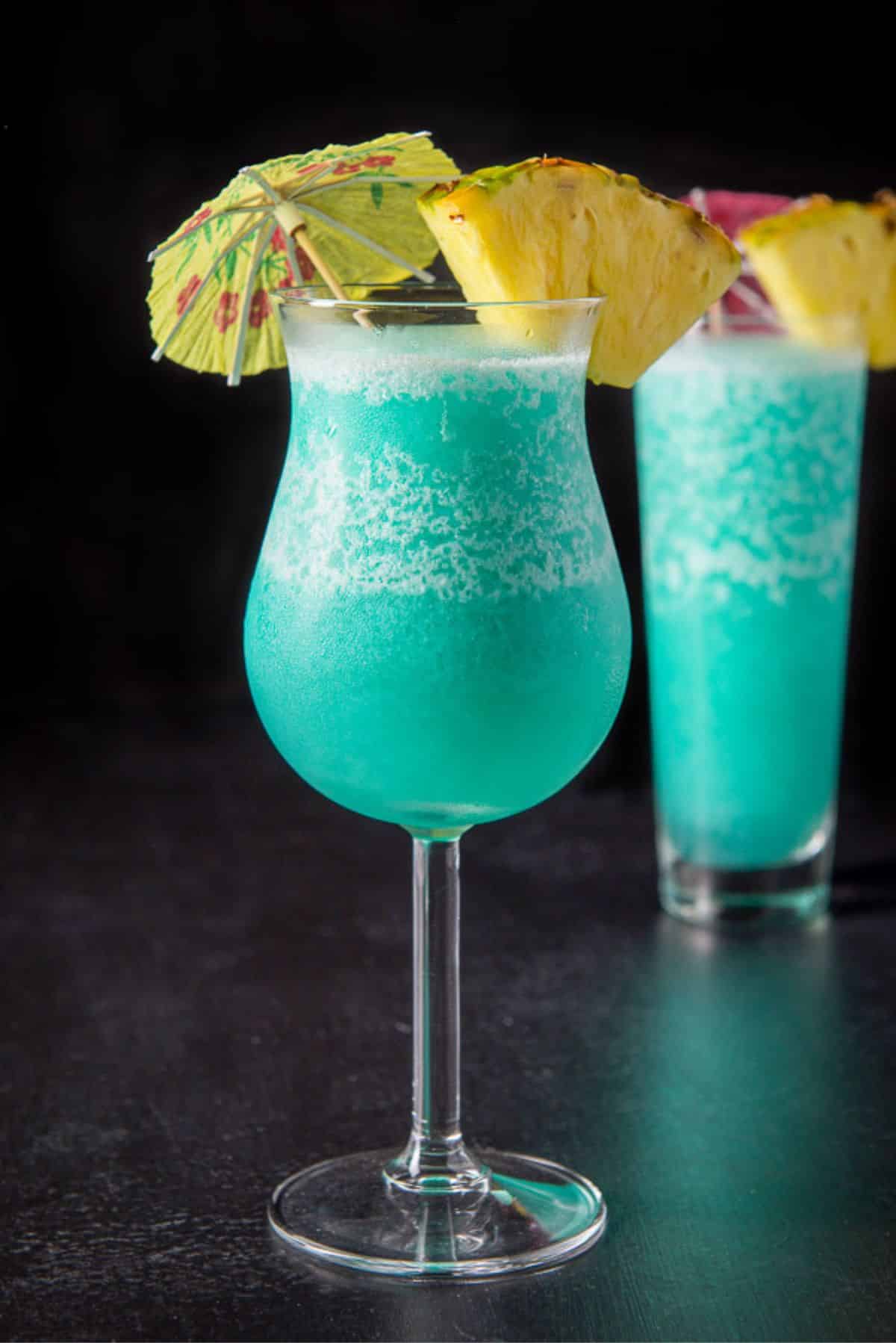 Vertical view of the cocktail in the tulip glass with the fruit garnish and the tall glass behind it